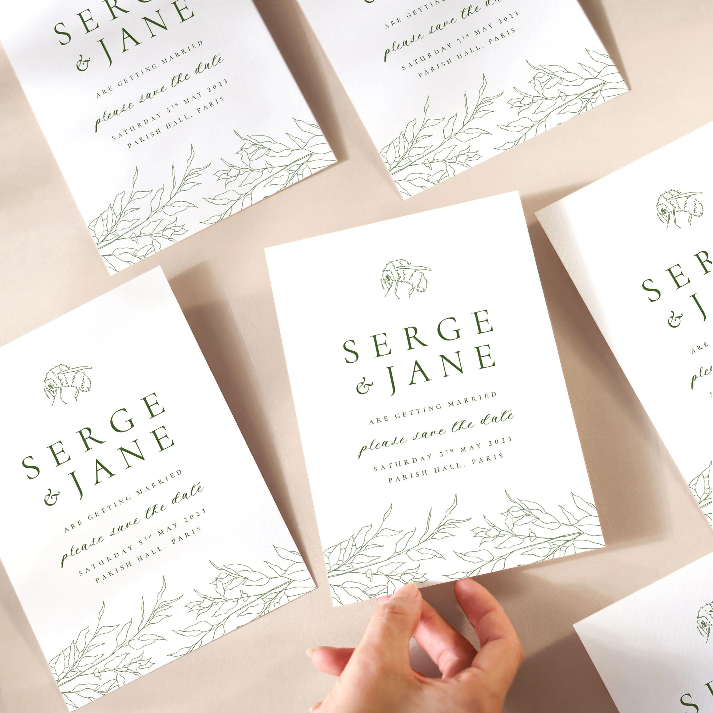 A hand picking up a save the date card with a delicate blue sketch and dusty blue serif text and a bumble bee illustration at the top.