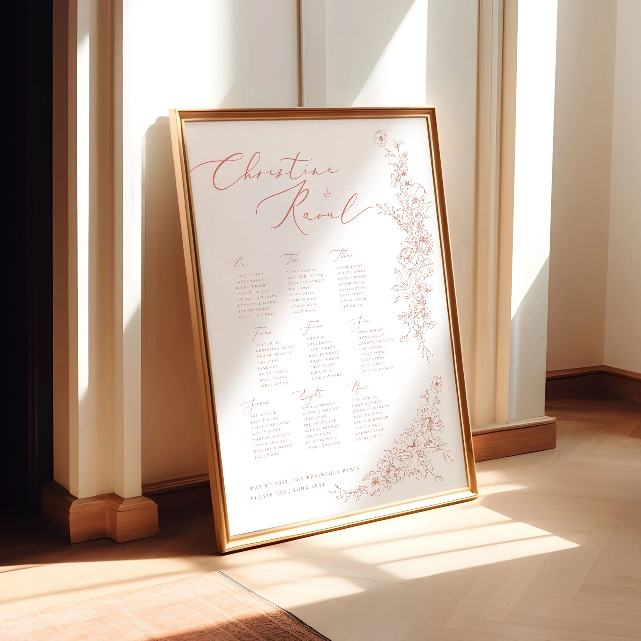 A framed A1 table plan sign leaning against a wall as the light spills across. The design has delicate hand drawn flowers in a blush pink colour.