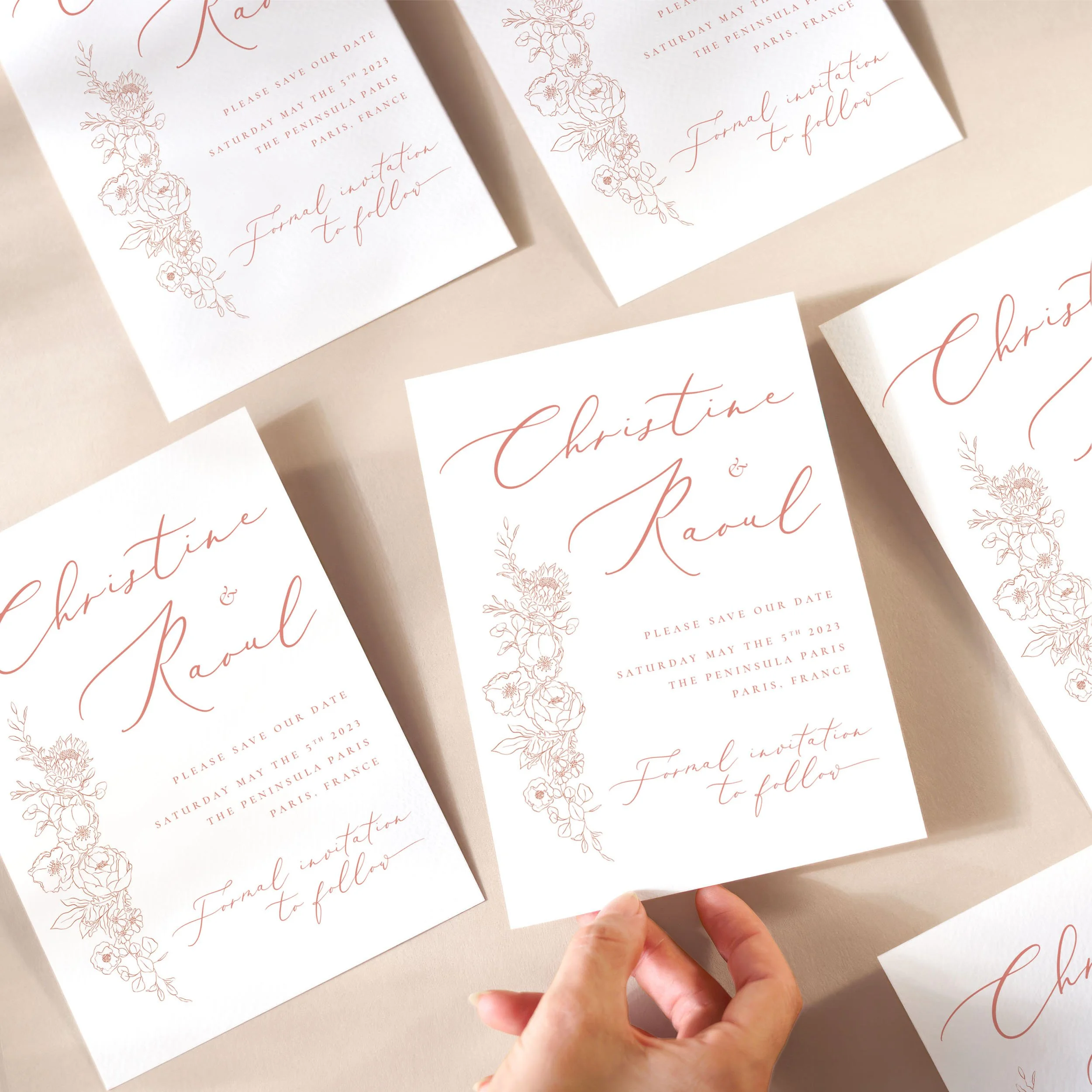 A hand picking up a save the date card with delicate pink flower sketches and pink calligraphy text.