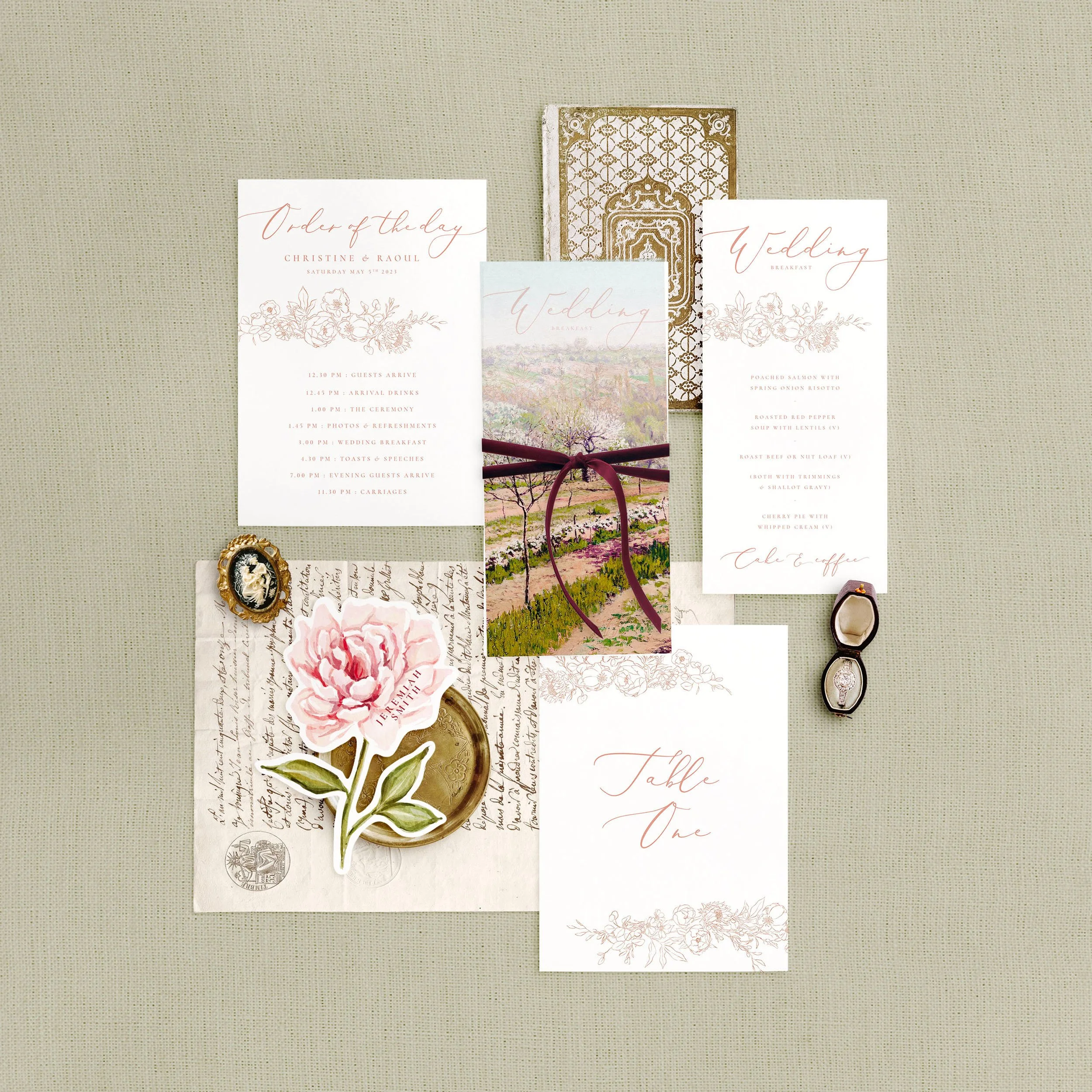 Wedding stationery flat lay featuring a menu, table number, order of the day and a peony shaped place card. Each has a delicate blush pink floral design.