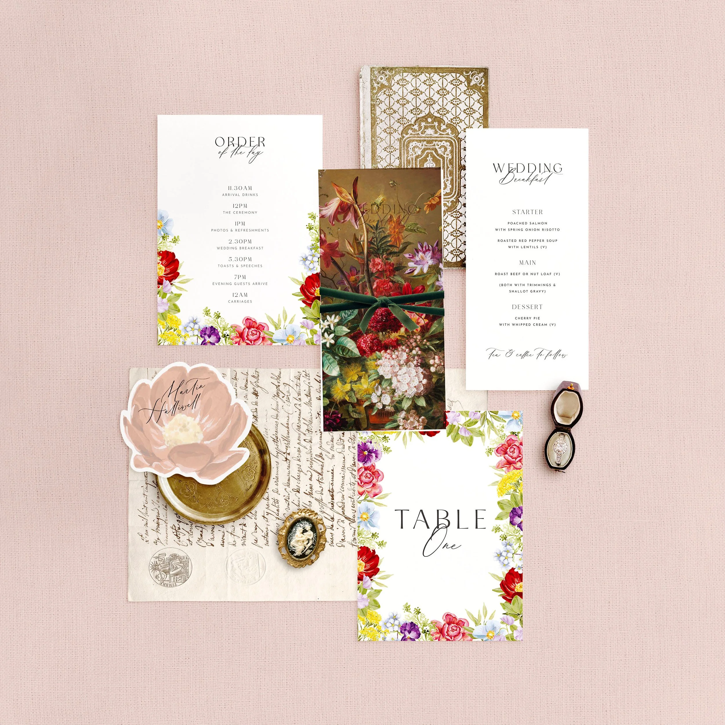 Wedding stationery flat lay featuring a menu, table number, order of the day and a flower shaped place card. A colourful floral design is on each card.