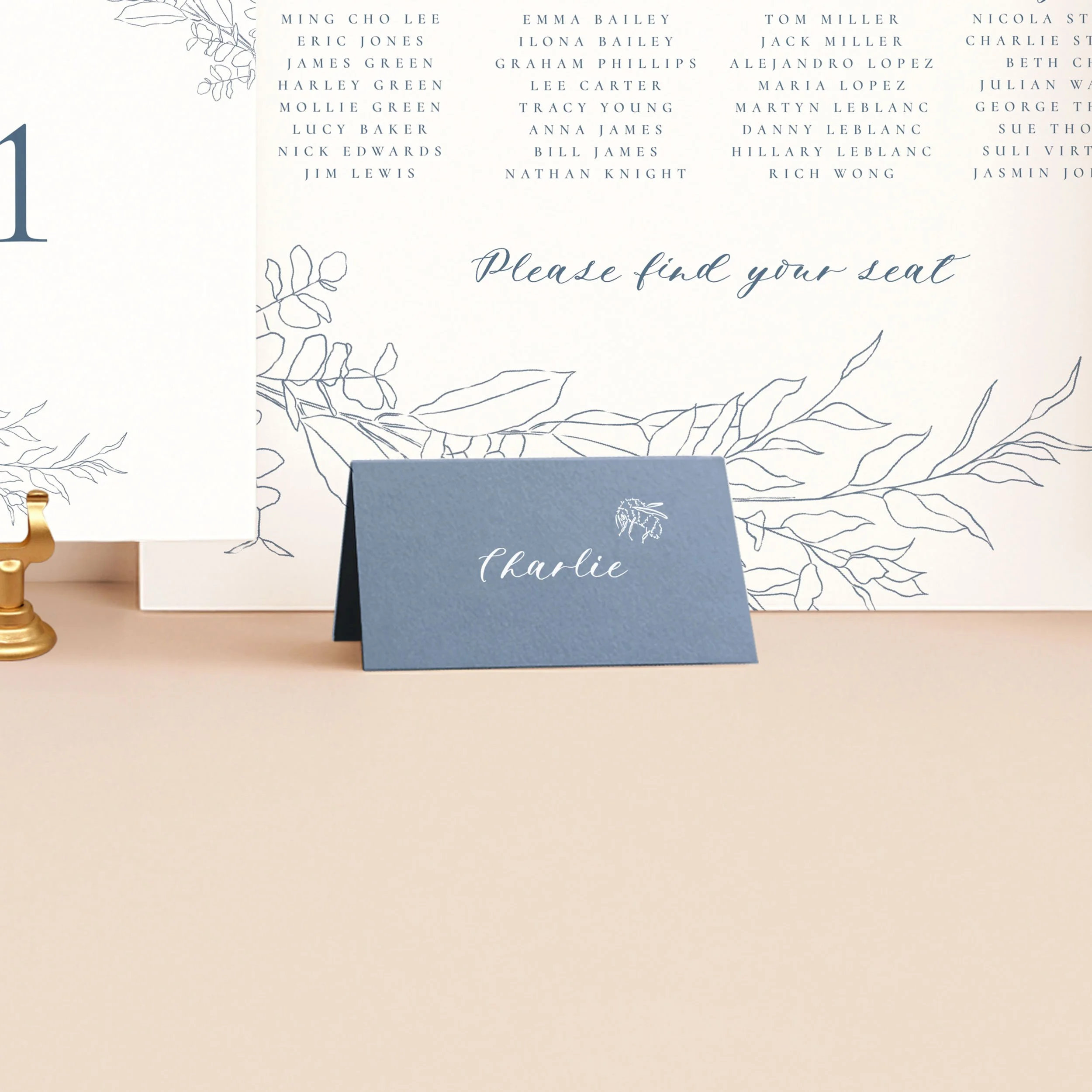 A rich dusty blue tent place card, printed in white ink with a guest name and a small bee illustration.