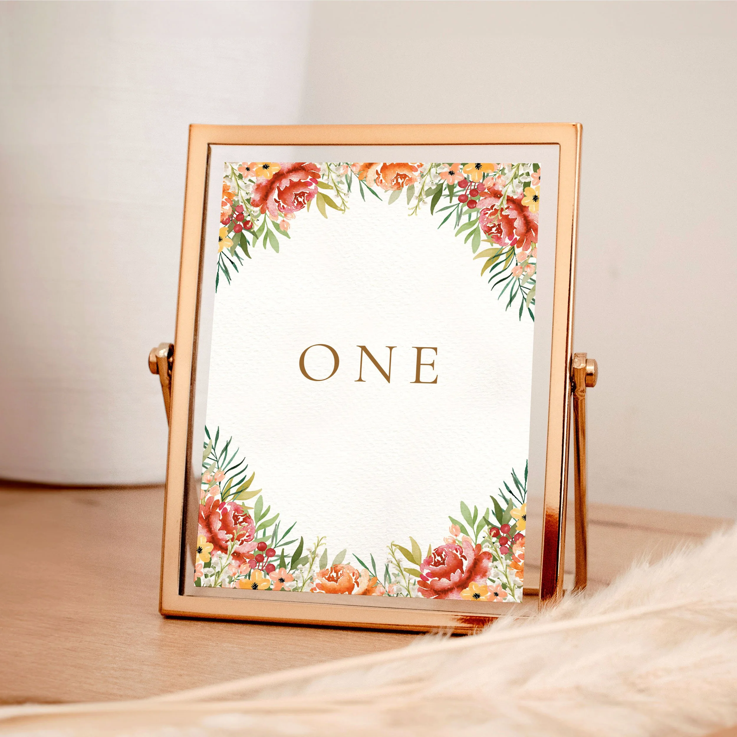 A table wedding number card in a rose gold frame with burgundy, yellow and orange watercolour flowers framing the design at the top and bottom.