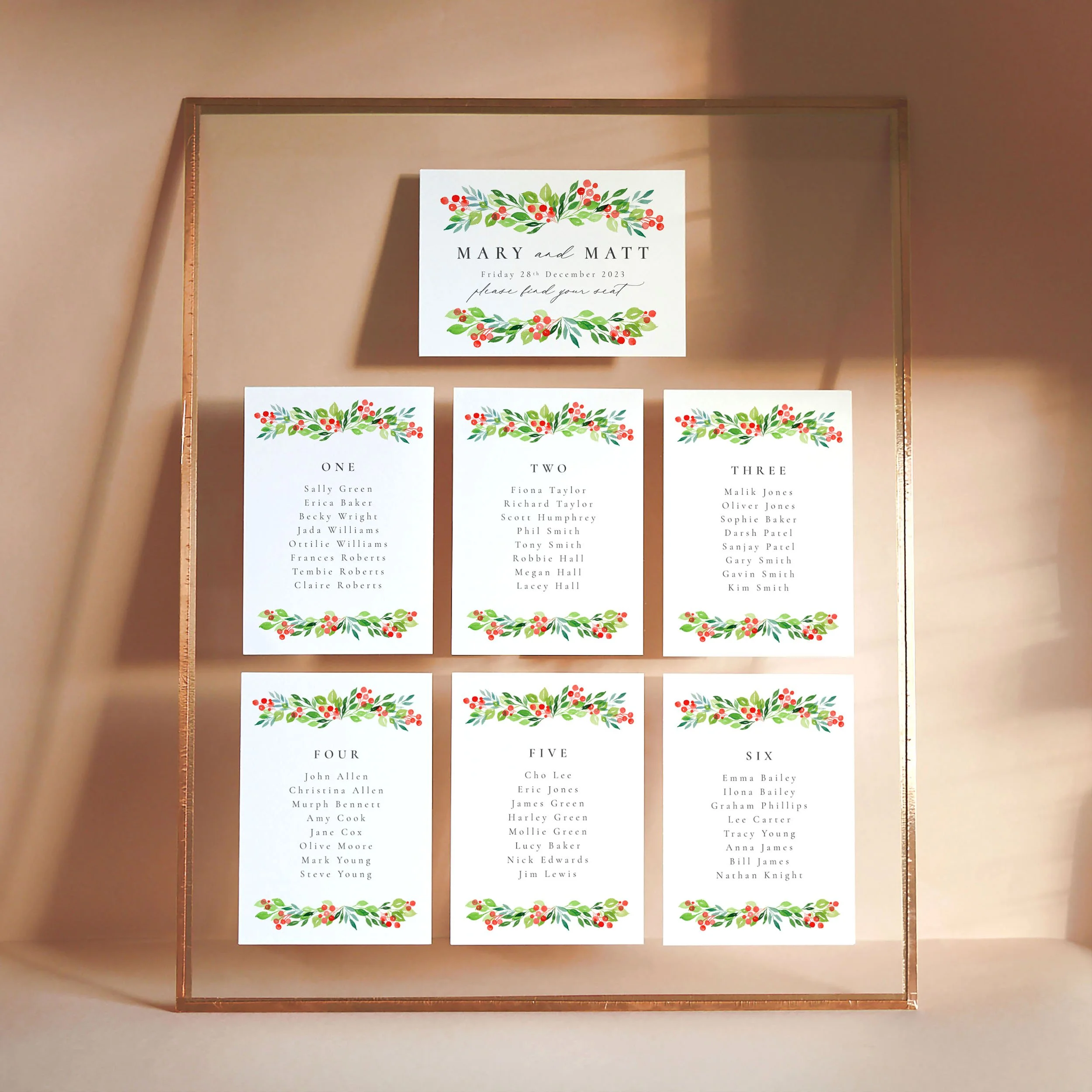 A set of small A6 printed table plan cards in a glass frame with copper edges. The design has watercolour green leaves and red winter berries.