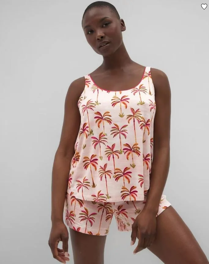 A woman wearing a sleeveless top and shorts with a pink background and a palm tree pattern, standing against a plain white background.