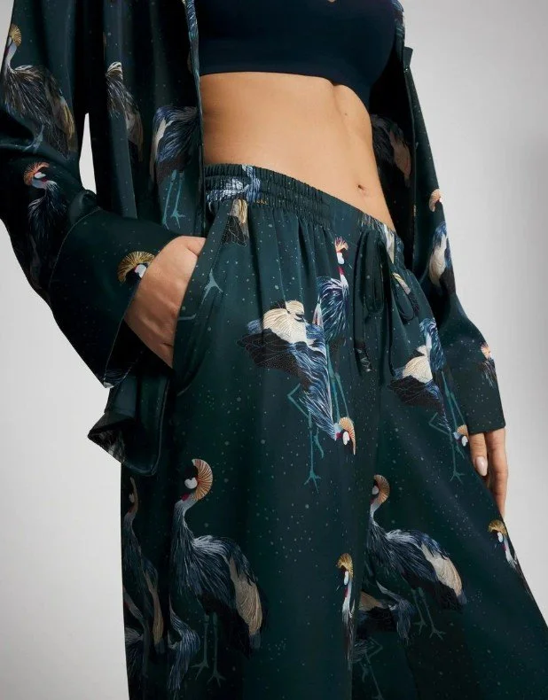 Close-up of a woman wearing black wide-leg pants with a crane pattern, a black crop top, and a matching pajama top with cranes on a starry background.