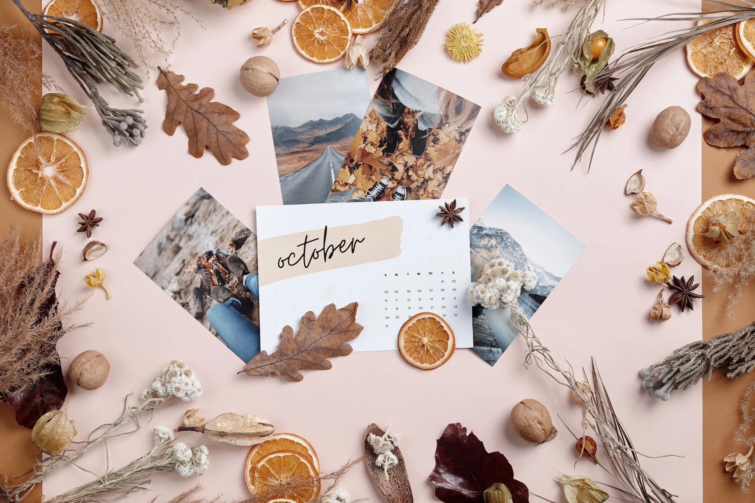 Flatlay of October calendar with autumn leaves, dried fruit, and plants on a beige background.