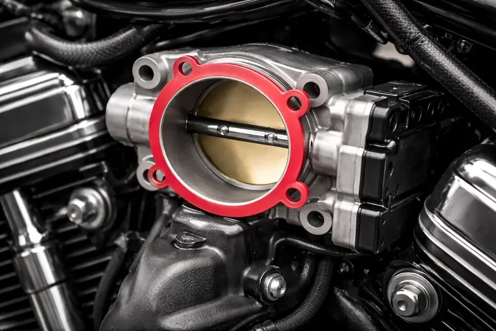 Motorcycle throttle body with red gasket installed between throttle body and intake manifold.