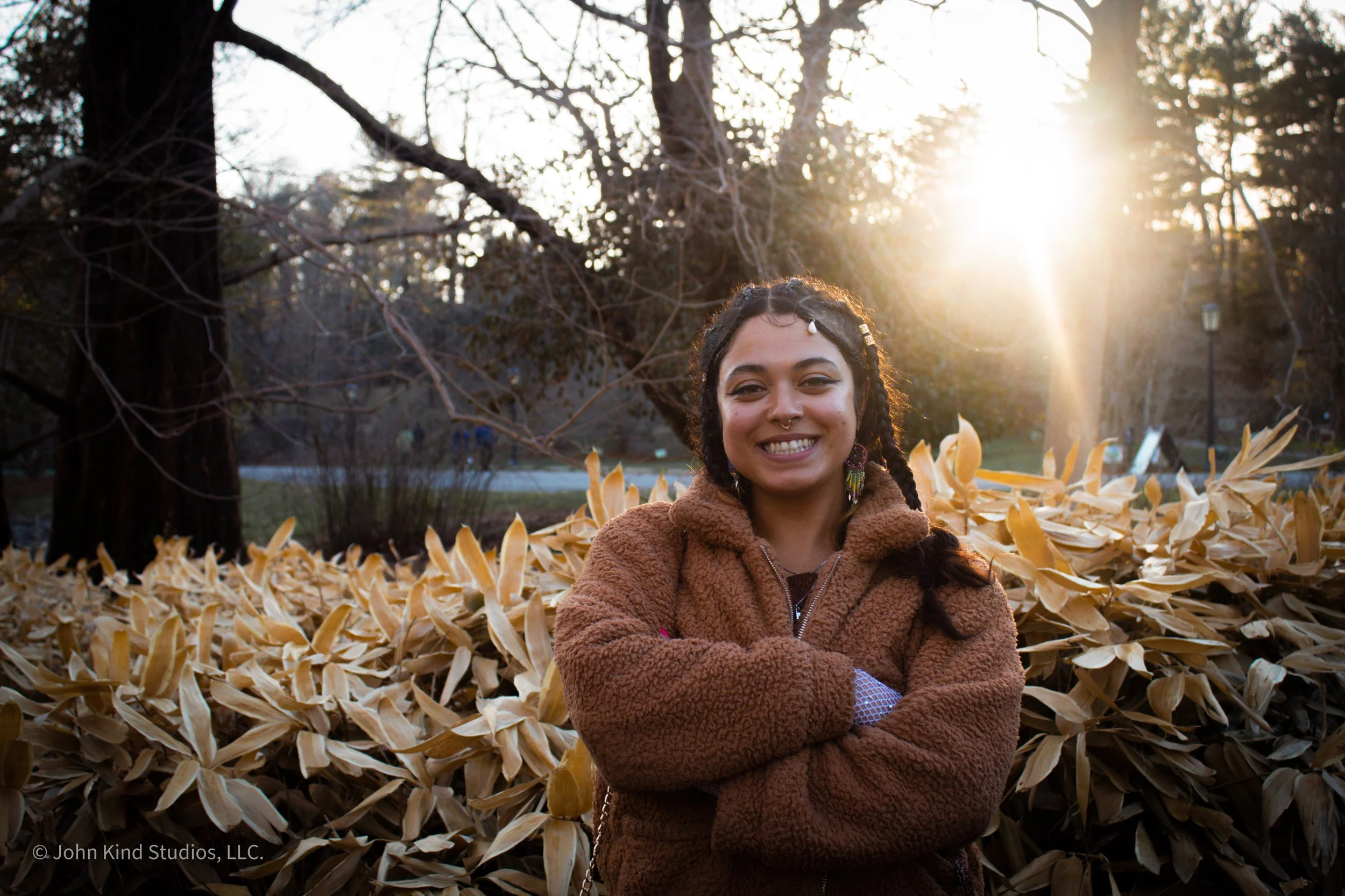 Artist Eva Davenport smiling with her arms crossed during an outdoor sunset portrait session photographed by John Kind Studios.