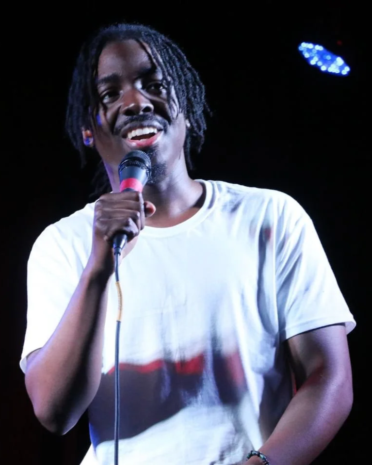 john kind on stage with microphone at a live event hosting and performing poetry