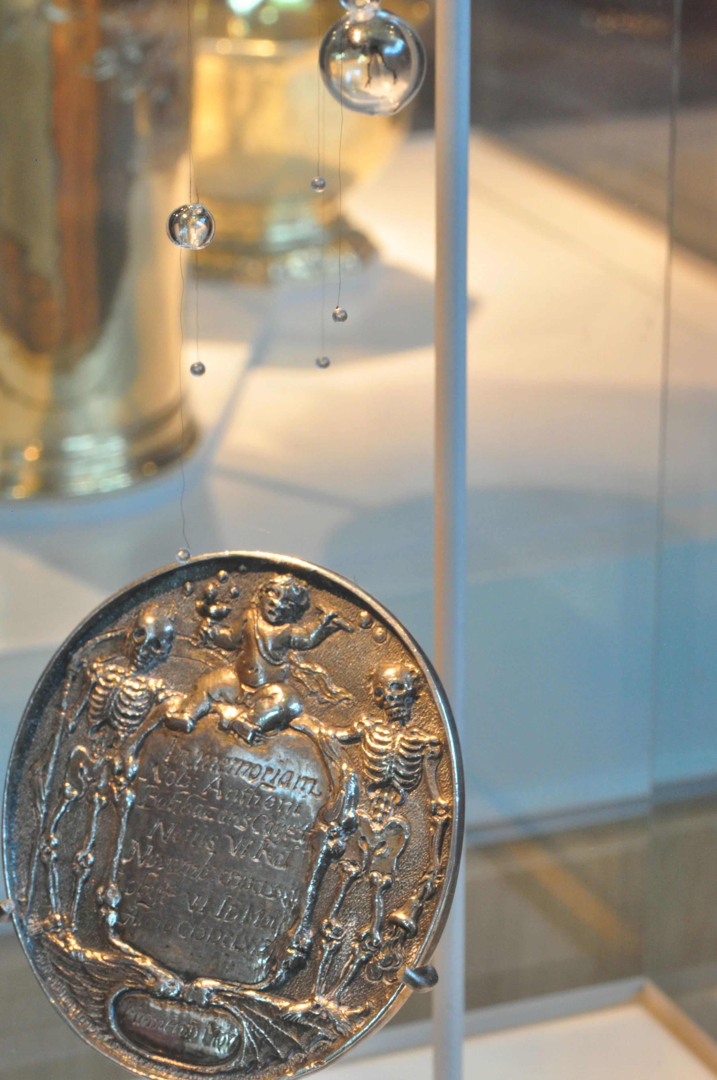  Bat winged fairies dance with dressed fleas&nbsp;below a silver memorial medallion. Floating upwards in bubbles the fairies are drawn towards Elizabeth Boser's funeral spoon. 