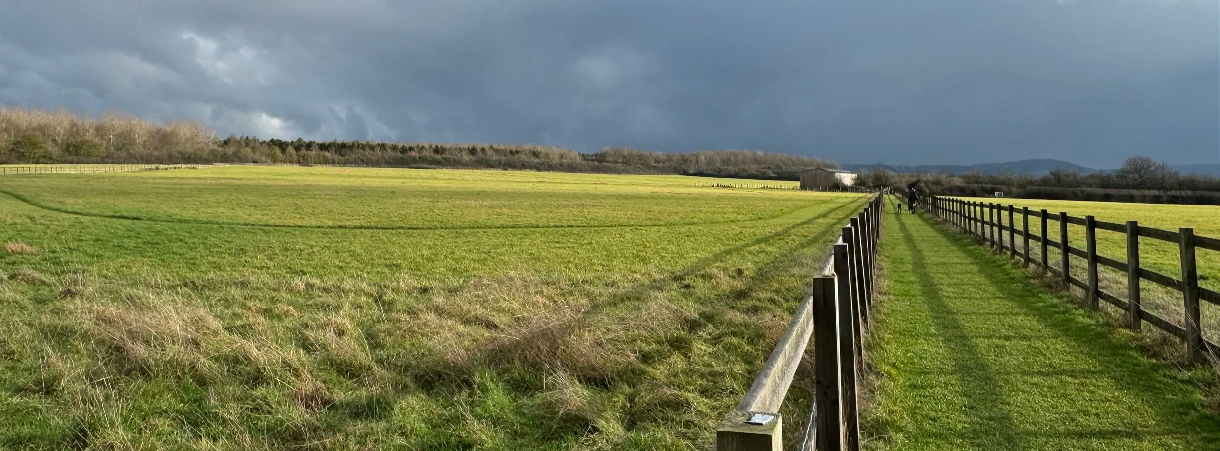 A fenced footpath leading across a field with the Chiltern hills in the background and grey skies