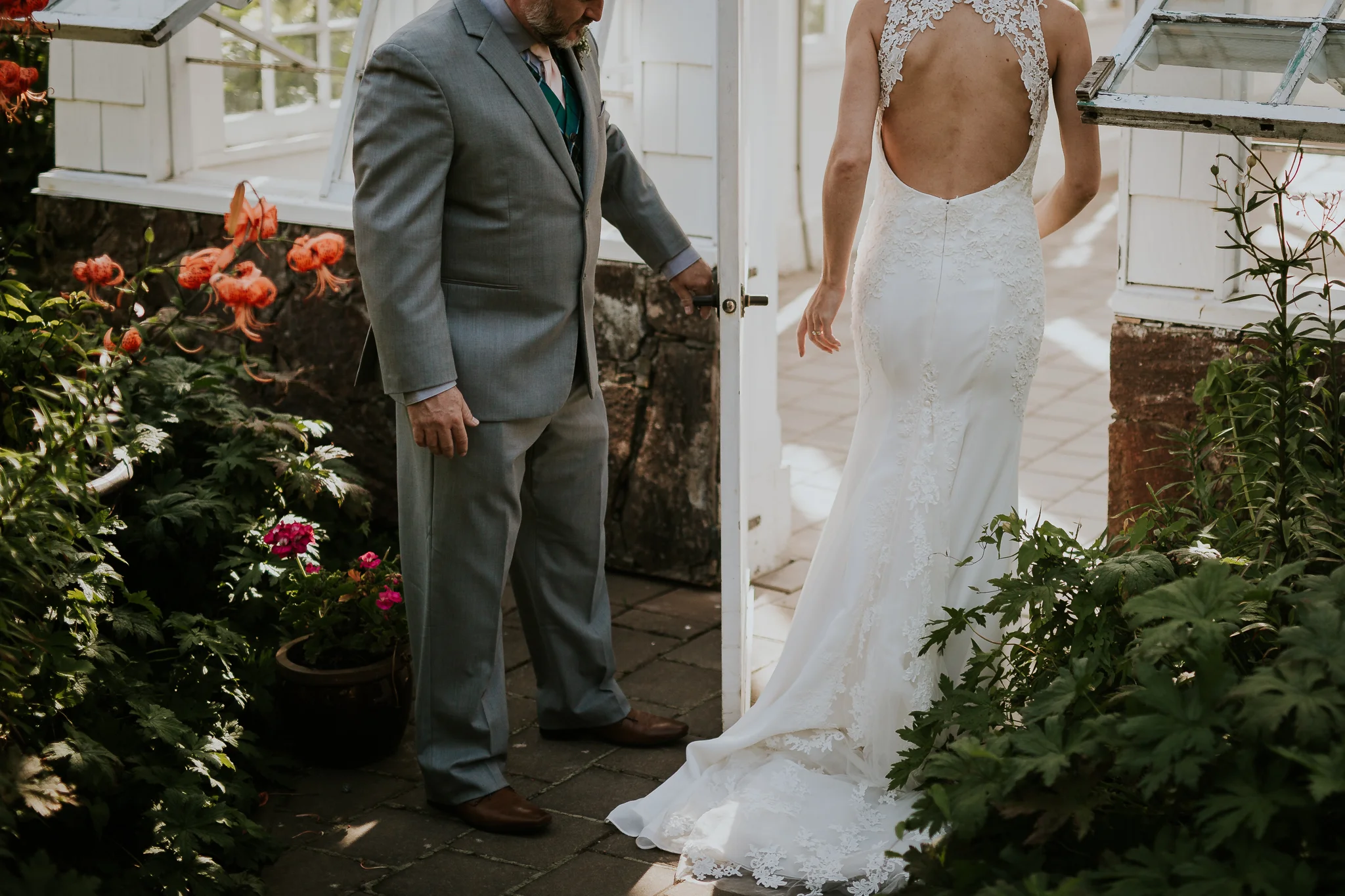 Groom holding brides dress while she walks into greenhouse for wedding photos near Victoria BC