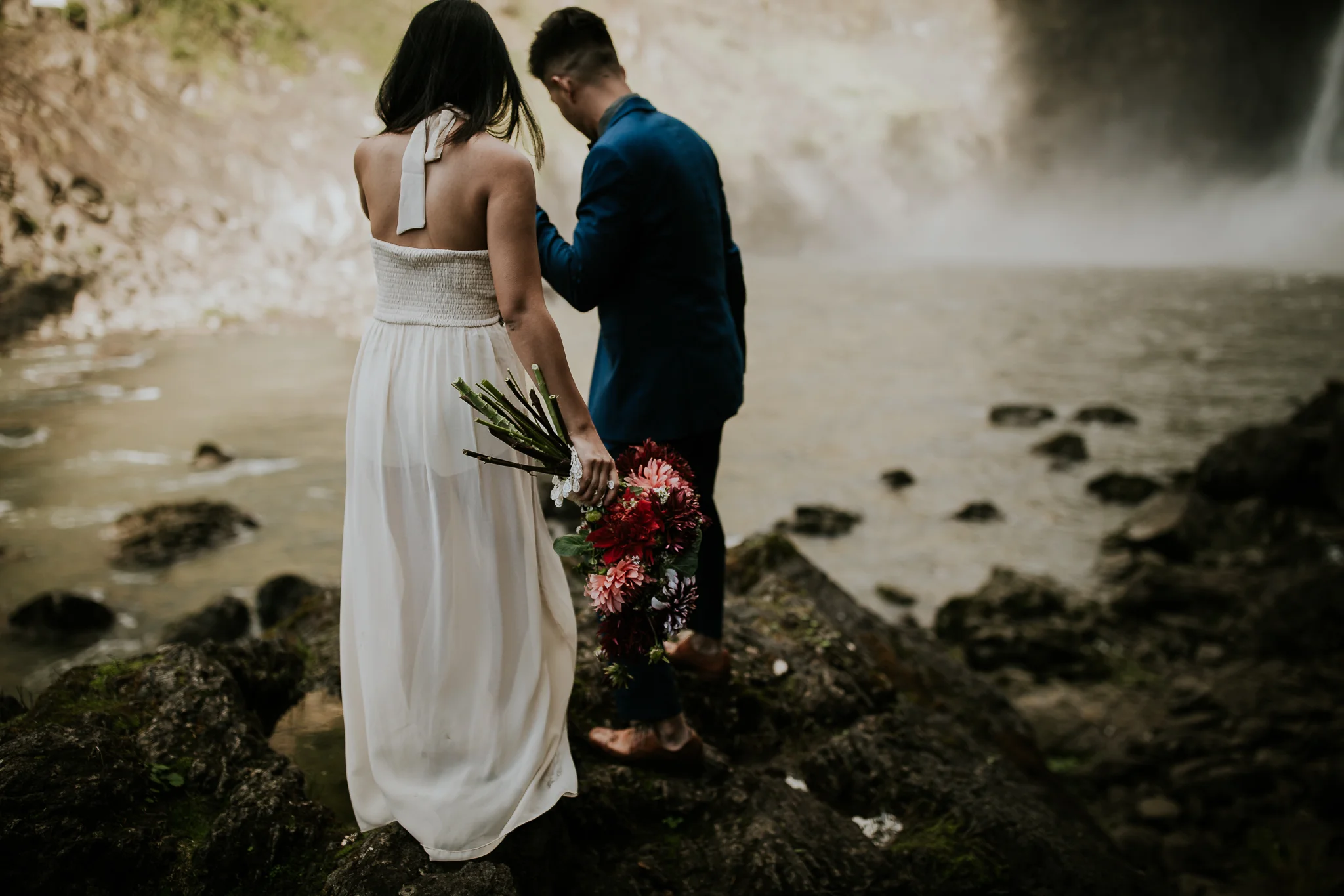 Groom leading bride across rocks to waterfall elopement