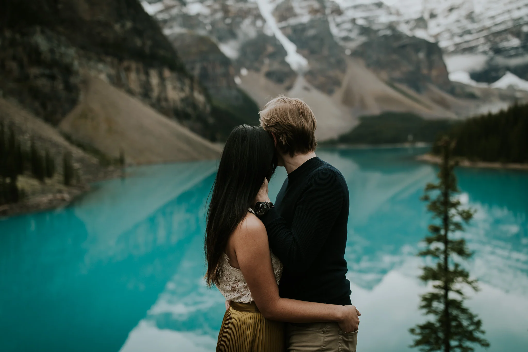  newly engaged couple embrace each other and look out at the blue of moraine lake during sunrise destination engagement session 