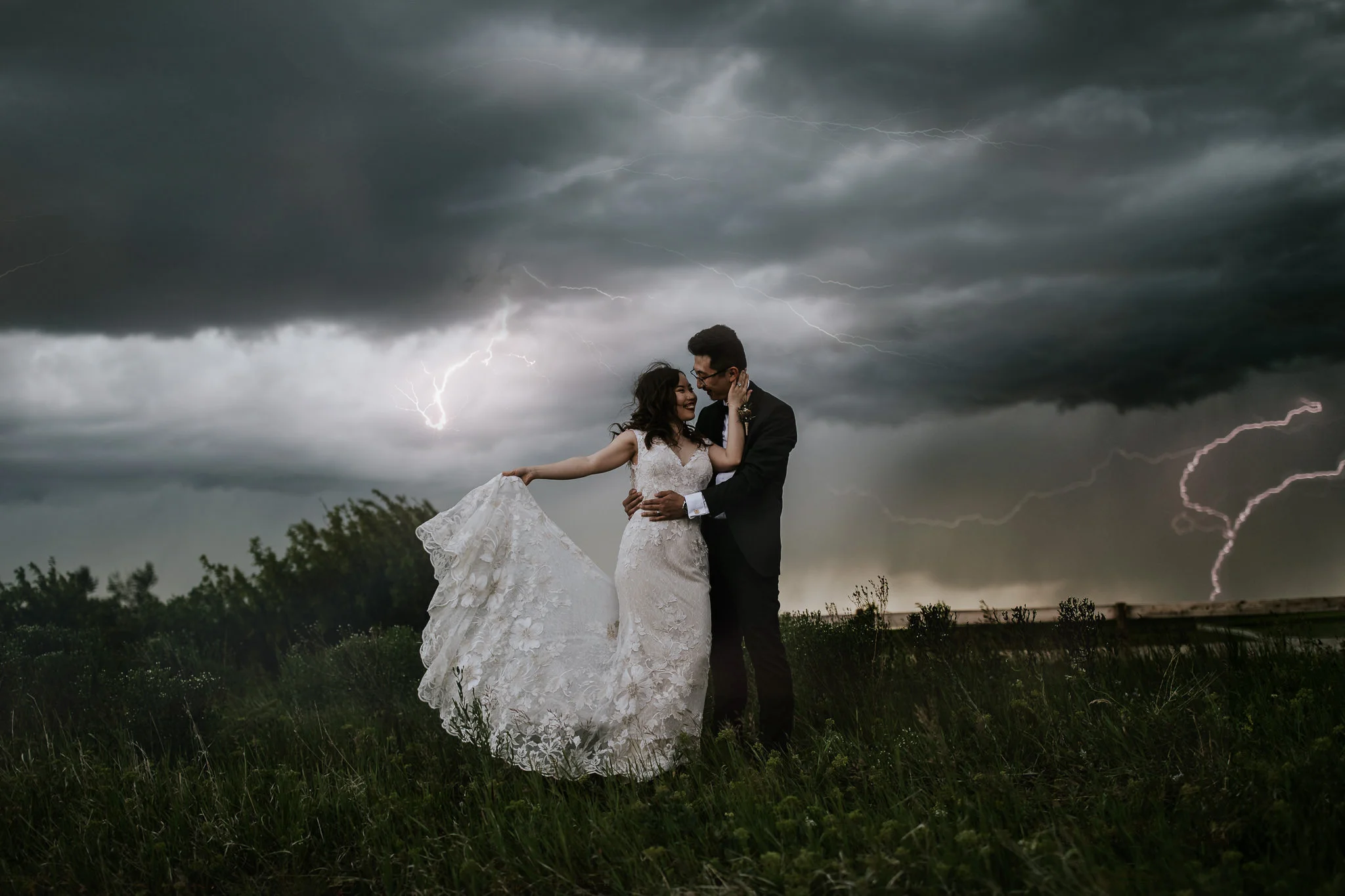  bride and groom embrace and bride holds out dress as lightning flashes in the background during destination wedding  