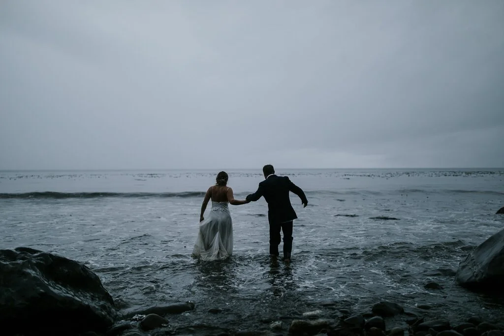  bride and groom holding hands and walking into the ocean at sunset during destination wedding  