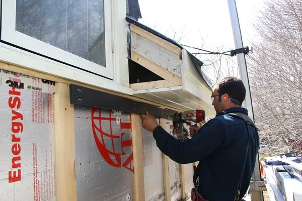 Pollard installs Cor-A-Vent SV-3 siding vent to the wall top before installing the frieze board beneath the soffit. He leaves a three-eighths-inch gap between the vent strip material and the thin thick furring strip. This gap will allow air to exhaust from the rain screen wall assembly, through the SV-3, and then between the frieze board and clapboard siding to be installed later.