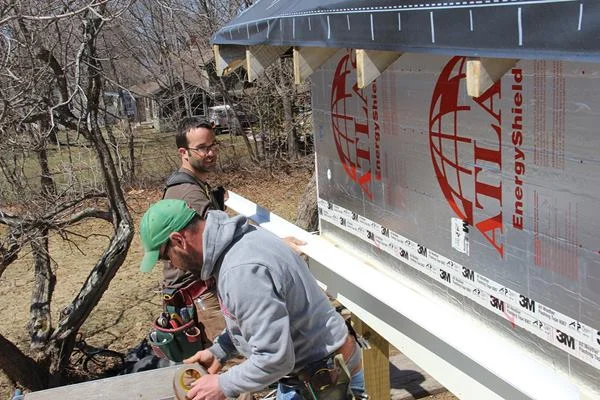 Pollard places a piece of aluminum drip cap flashing over the porch beam fascia. An air inlet and drain opening for the upper portion of the wall siding assembly will be installed at this location.