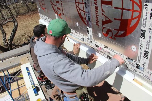 Fenton removes the paper backing from the tape as Pollard lines up the flashing and adheres the top edge of the tape.