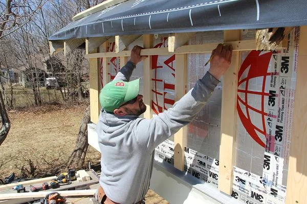 Shane Fenton positions a 2x ledger over the wall furring as nailing for the soffit of the roof eave overhang. The air space built into the wall will extend up into the eave cavity.