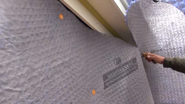 Pollard slices the Mortairvent fabric to fit with a utility knife. Thompson Johnson likes Mortairvent because it lies flat on the wall and is manufactured by a local Maine company (Advanced Building Products, Inc., of Springvale, Maine).