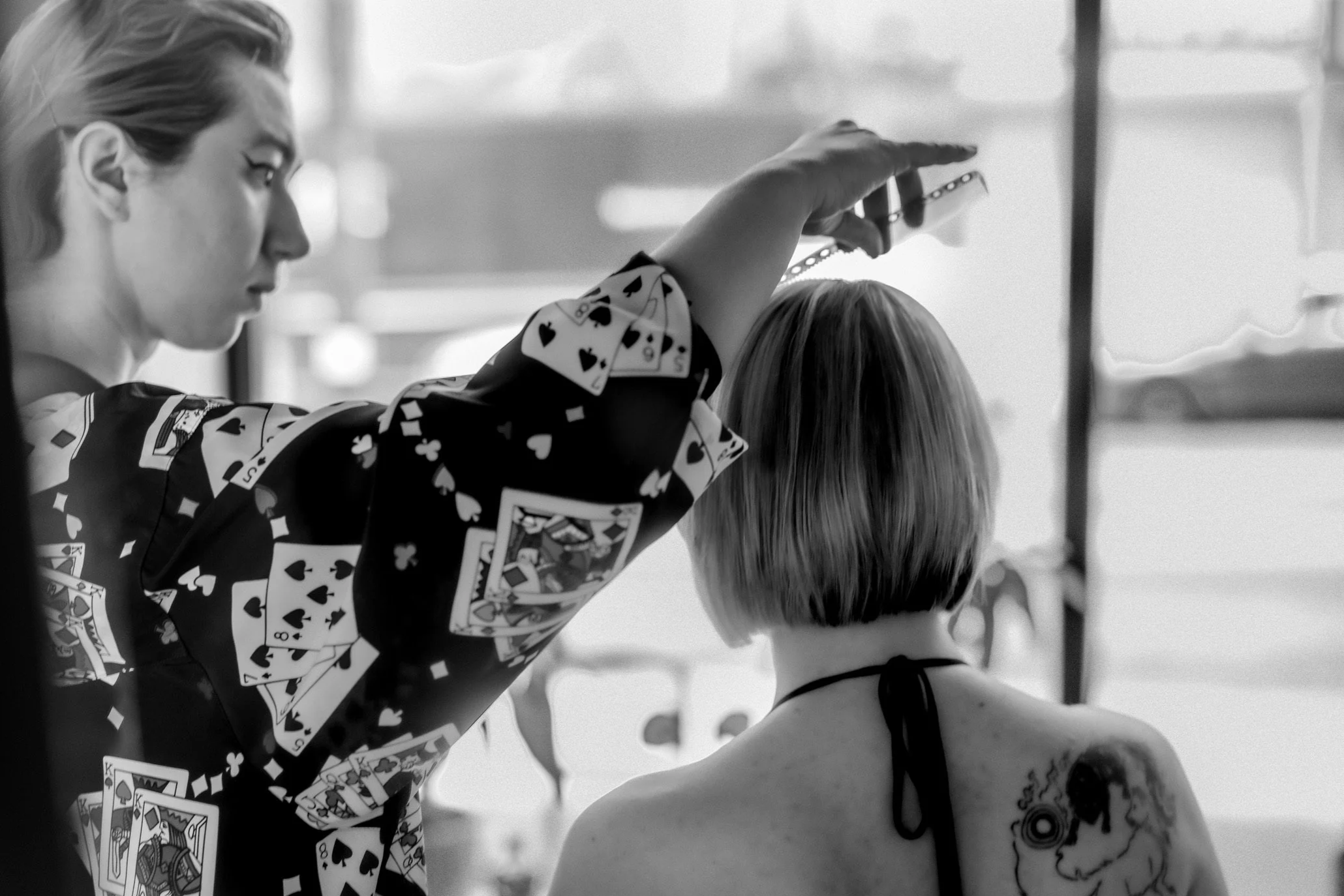 A person in a vintage shirt with playing card patterns is combing a persons hair, in an indoor environment.