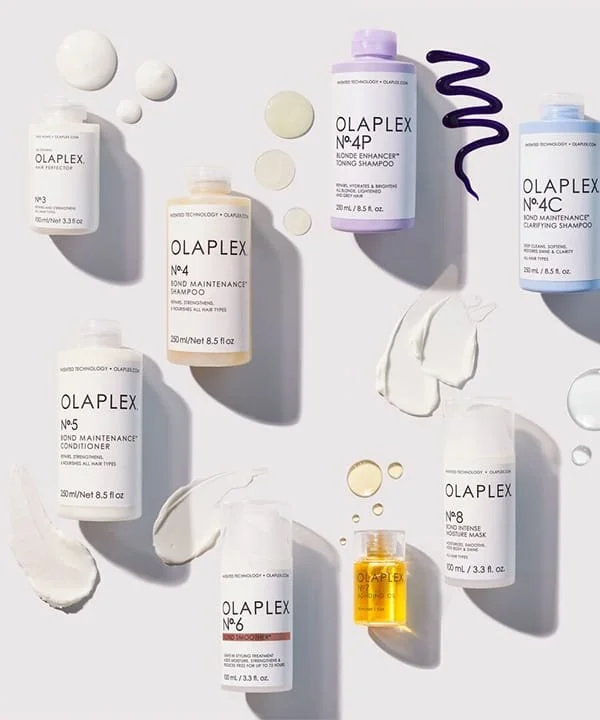 Collection of OLAPLEX hair care bottles with swatches and splashes of product on a light surface.