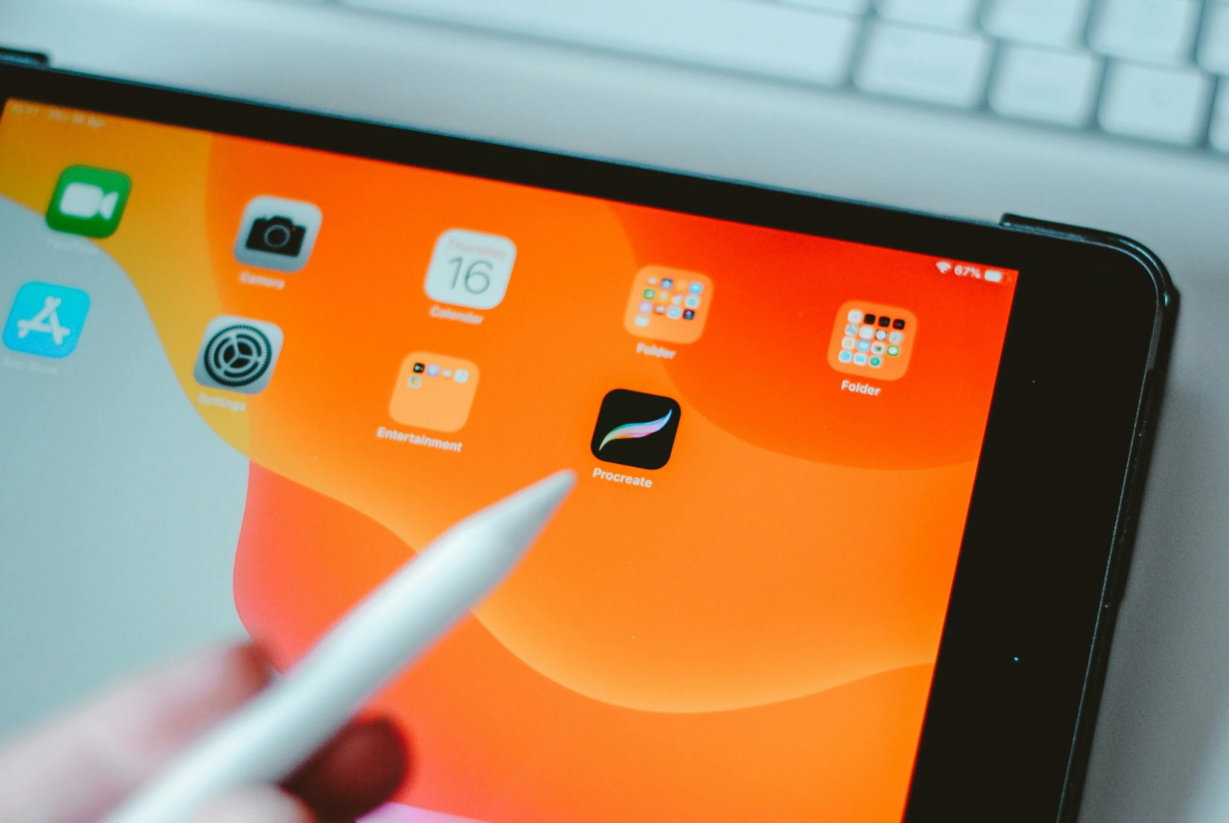 Close-up of an iPad screen with app icons, including Procreate, two folders, and other apps, with a stylus being used to interact with the screen.