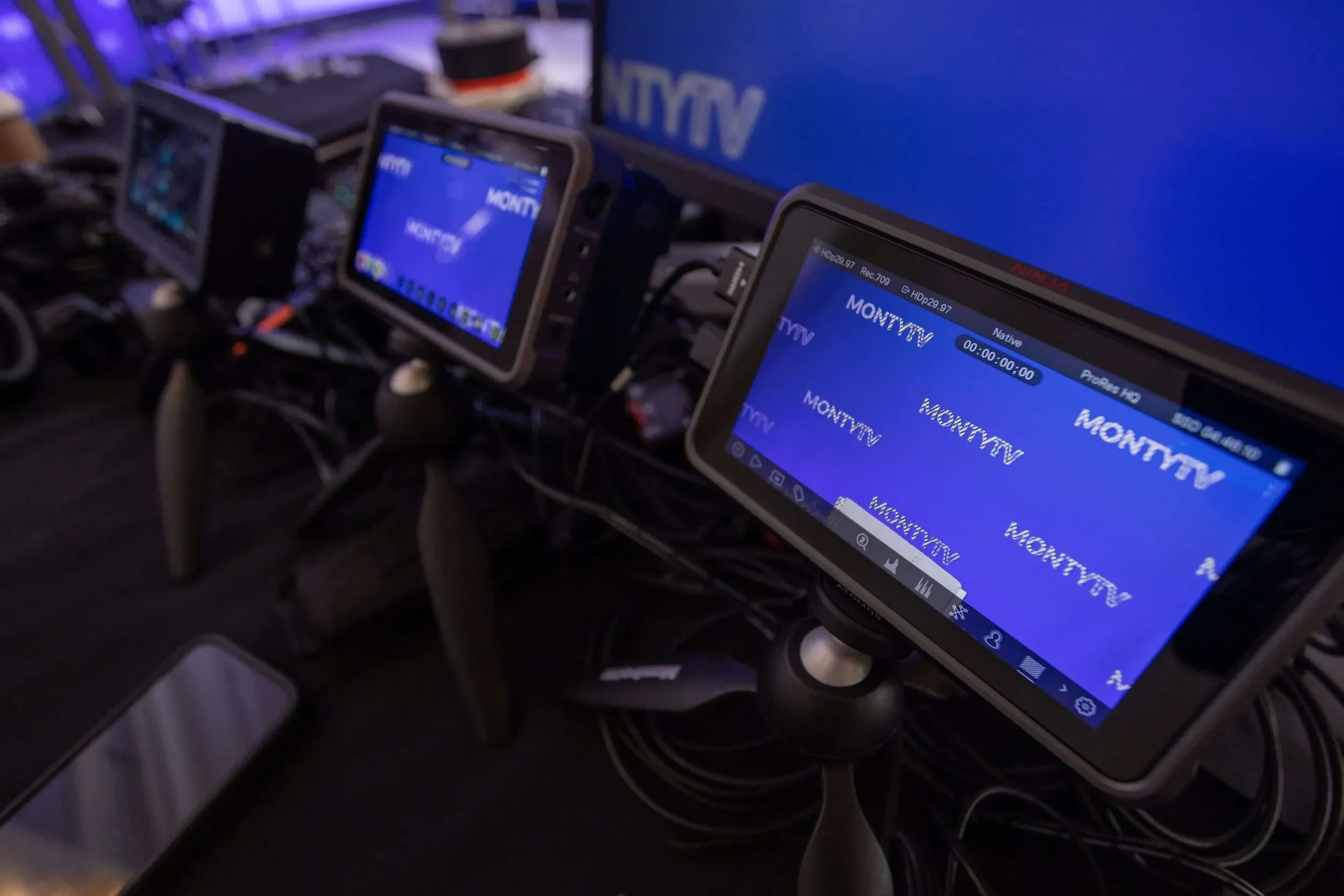 Multiple monitors displaying the 'MONTTV' logo, set up on a table with various cables connected, likely in a technical control room or broadcast station.