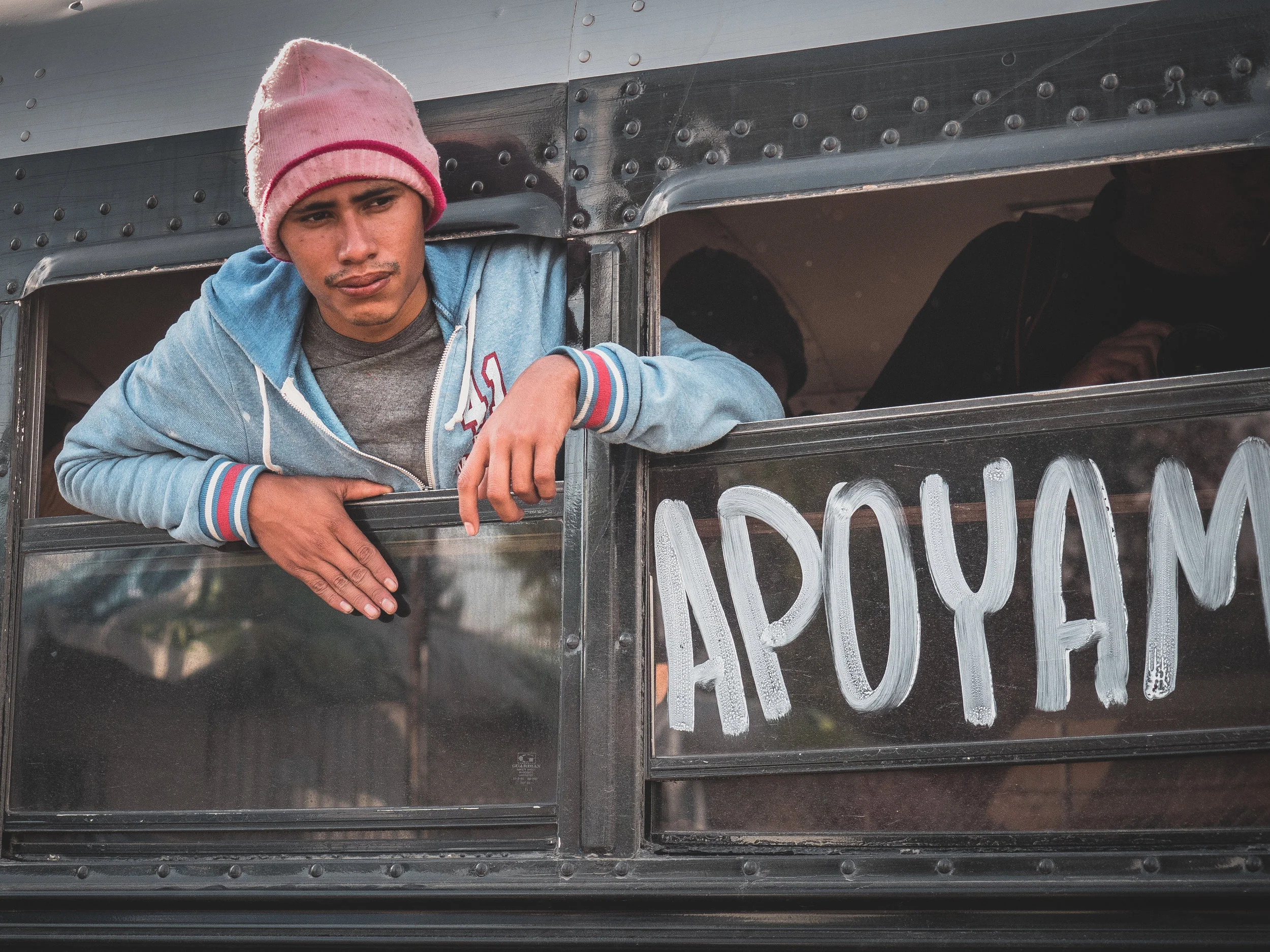 Apoyamos This photo shows a migrant caravan member as he departs on a bus for another shelter. While living conditions were reportedly much better in these secondary shelters, they were also more distant from the Mexican-American border (up to 45 minutes by bus). In this light, many migrants refused to leave the Benito Juarez sports complex due to its location in sight of the border. This bus is marked with the short message ‘apoyamos,’ which means ‘we support.’ I took this to mean that the migrants support each other, which was a theme I saw constantly exemplified during my short time at the camp. This migrant movement as a whole impressed me as extremely brave and struck powerful cords of human commonality and the arbitrary nature of political borders. I hope that this movement inspires international compassion in the coming years.