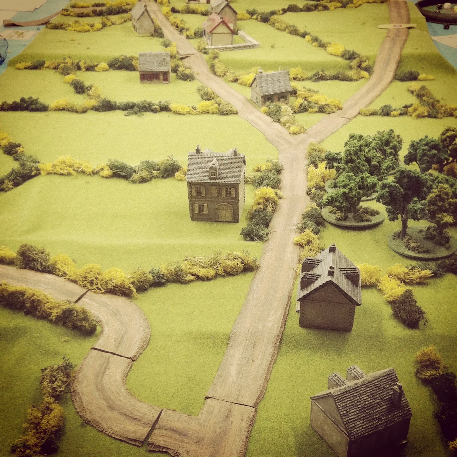 Scenario set-up with two small houses as objectives at the middle of the table set amid rolling hills, small farms and thick bocage