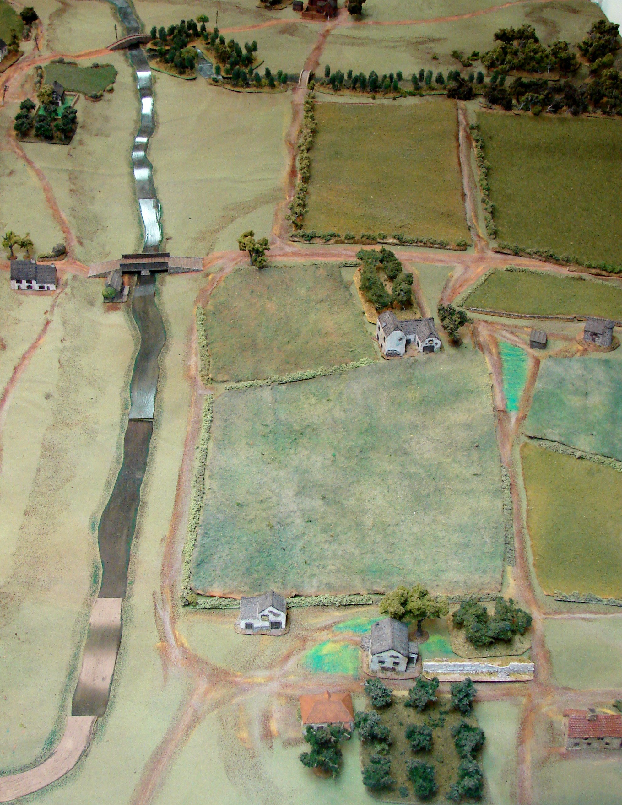 Overview south to north The center farm would be a nice place to defend, but the German player opts to only place one Pak there without infantry support, and put another ATG covering the smaller bridge to the south (also without support). The remaining Pak is in the village overlooking the center bridges. The infantry is all back on the left side of the stream. The British infantry is going to come on after the tanks along the road at the bottom of the picture, and manage to get all the way to the stream without being spotted.
