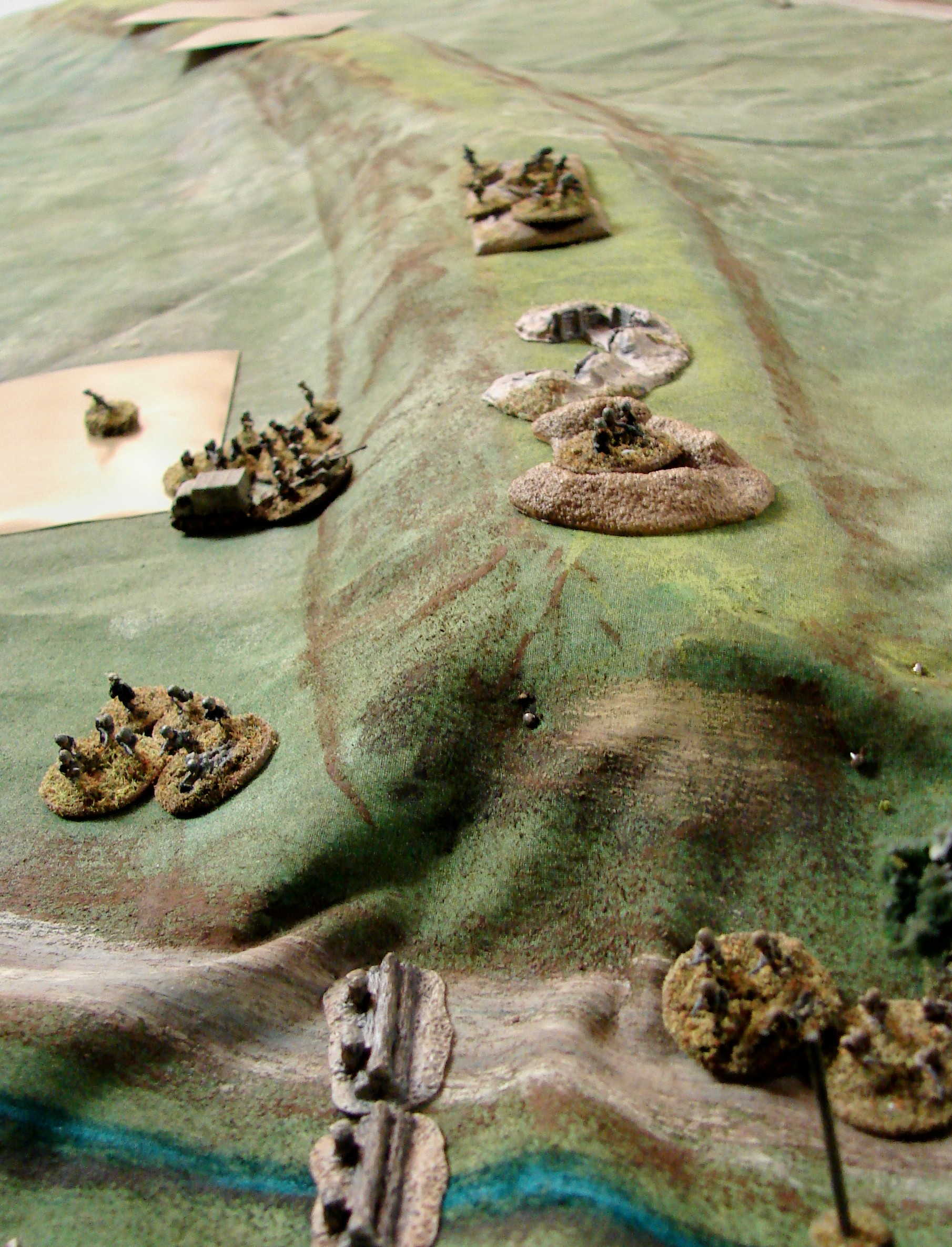 Defenders making some moves The surviving Pak crew drags their gun down to the RSO tractor. There is another pak & MMG team under the blind that moved up from the other dike. While the 50 cals took out the Pak crew and most of the MMG team, the Russian scouts managed to make it to the side of the dyke. Dennis sends his Big Man and 2 sections on a mission to assault the Russkies before they can get their breathe back. I need to figure out a way to get the cloth to lay flatter againt abrupt rises like this dyke. A couple of pins just ain't enough to hold down the fabric.