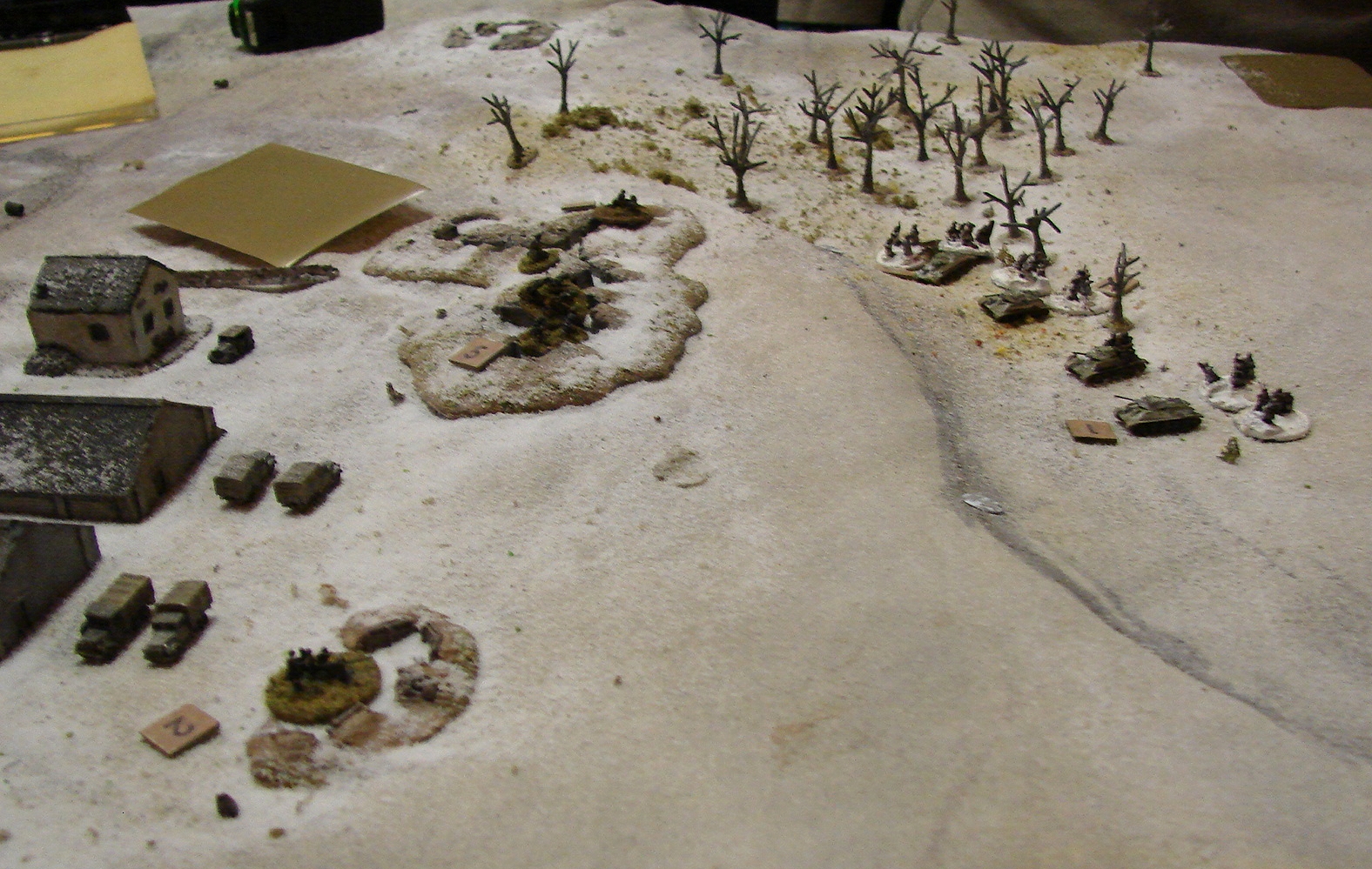 Opening Shots The first Soviet unit to appear was armor and some tank riders in the NW corner among some leafless trees. Four T-34s and a very weak company of infantry. They ran into fire from some entrenched troops, an MMG and a 20mm AAA gun. This shot is after fire has been exchanged and both sides have taken casualties. There is an 88 under the Blind to the left.
