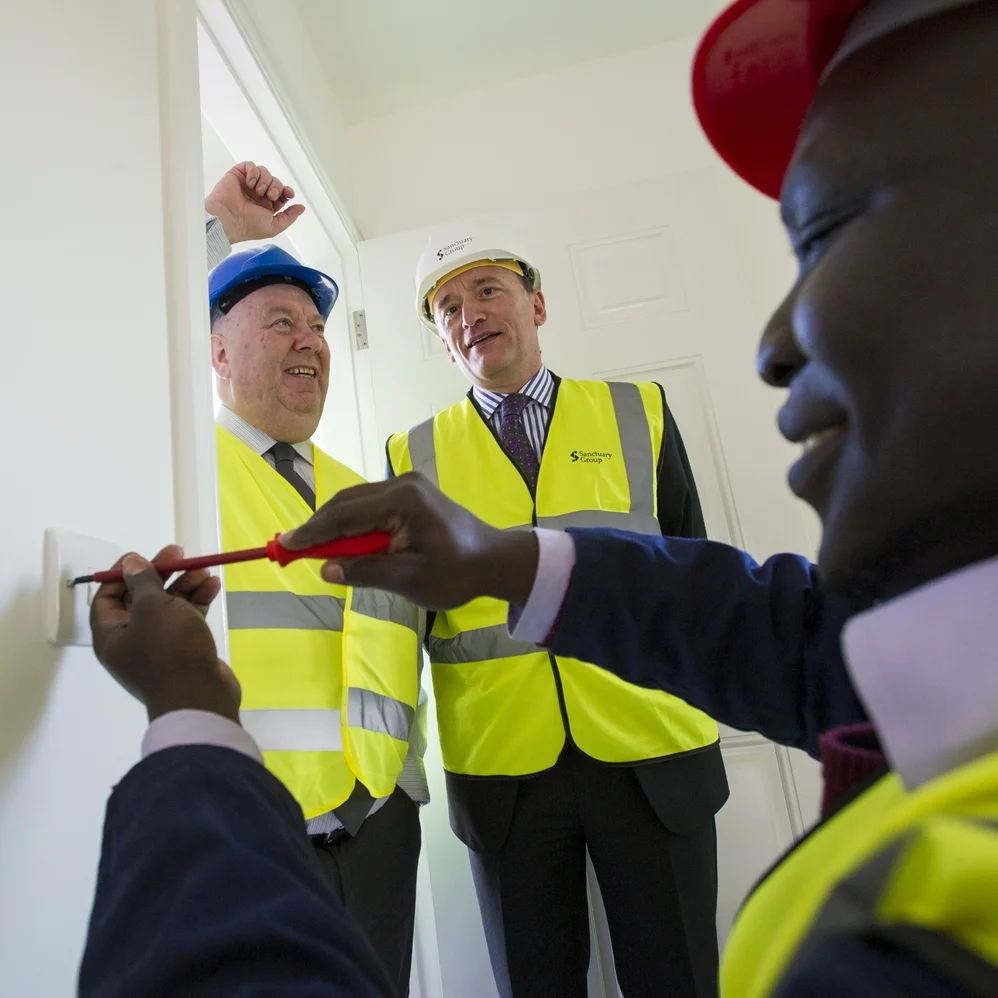 Mayor Joe Anderson and Sanctuary’s chief operating officer Ian McDermott look on as City of Liverpool College student Mani Mango undertakes some electrical work.