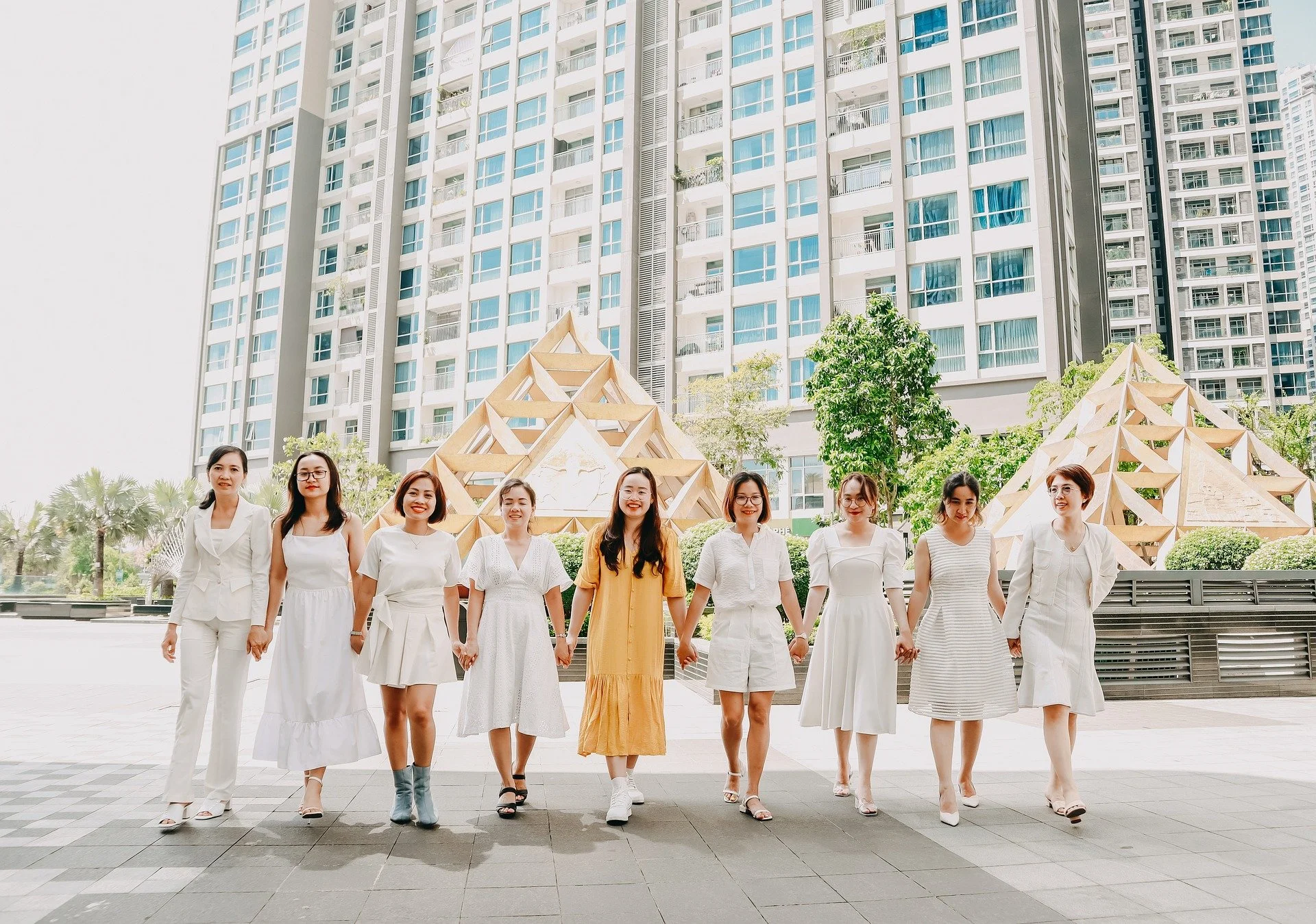 9 women holding hands in a line in front of a large building.