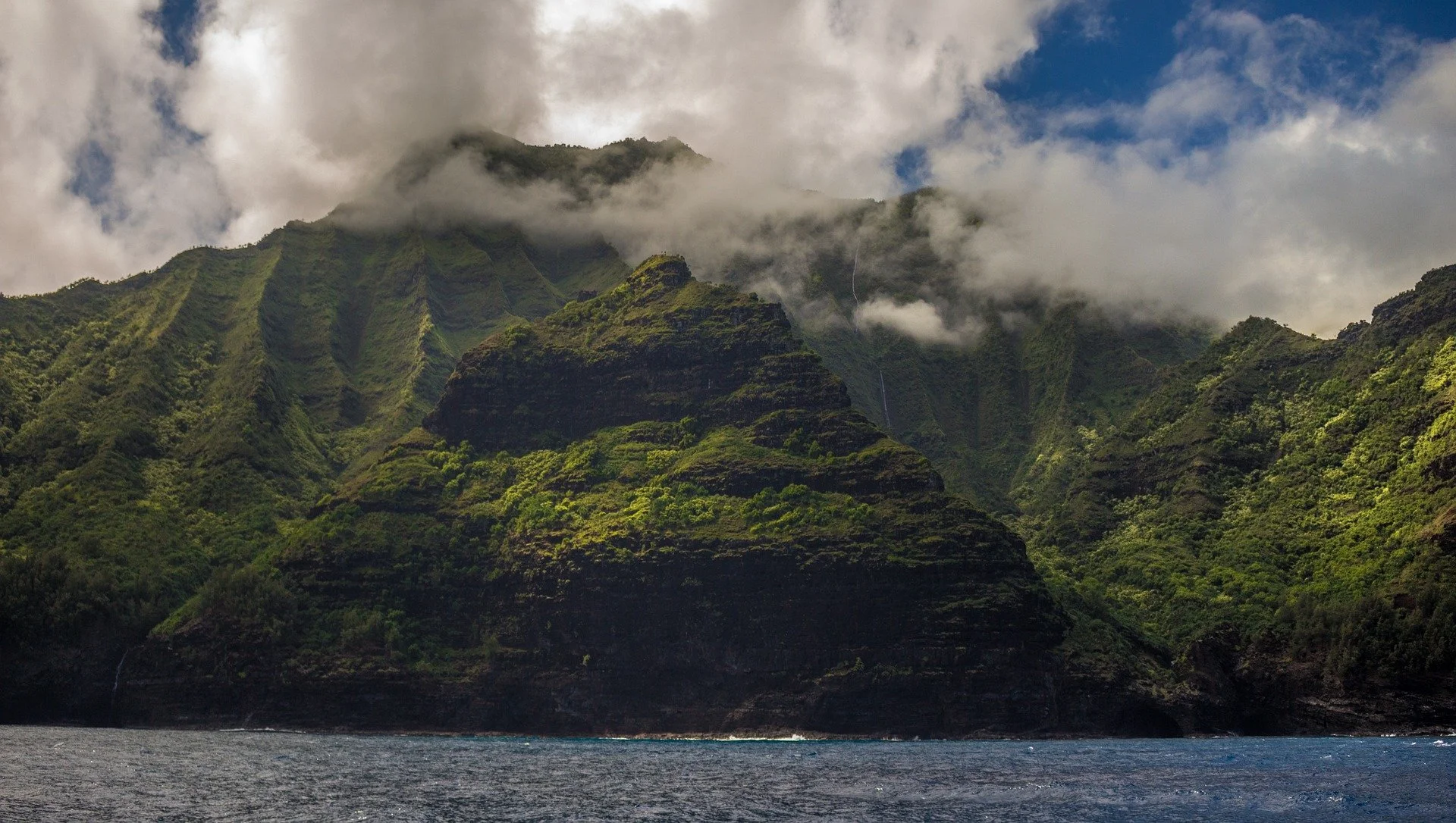 Green mountains and clouds next to the ocean