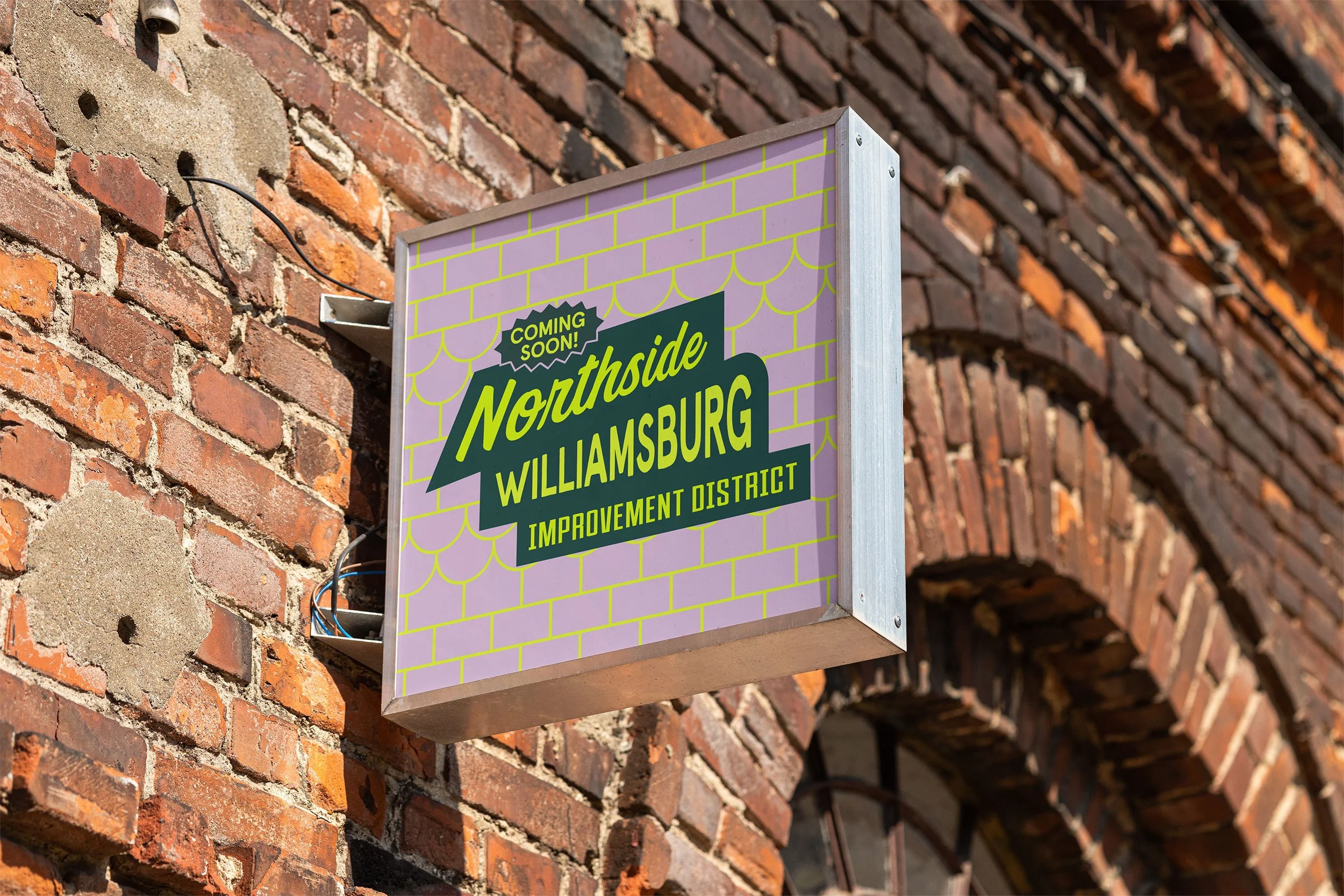 Mock-up of the Northside Williamsburg Business Improvement District branding on a street sign hanging on a brick building reminiscent of a Brooklyn building.