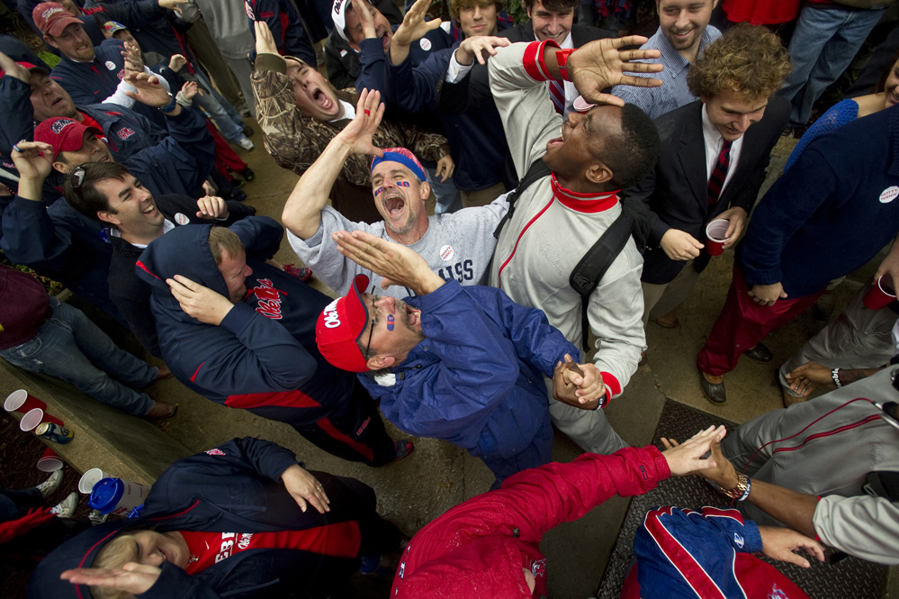 University of Mississippi football fans Darin Farley (bottom) and Todd Morris (top left) give the "Land Shark" fin salute with Rebels defensive end Jason Jones in "Whiskey Alley" during the team's Champions Walk parade through The Grove on the Ole M