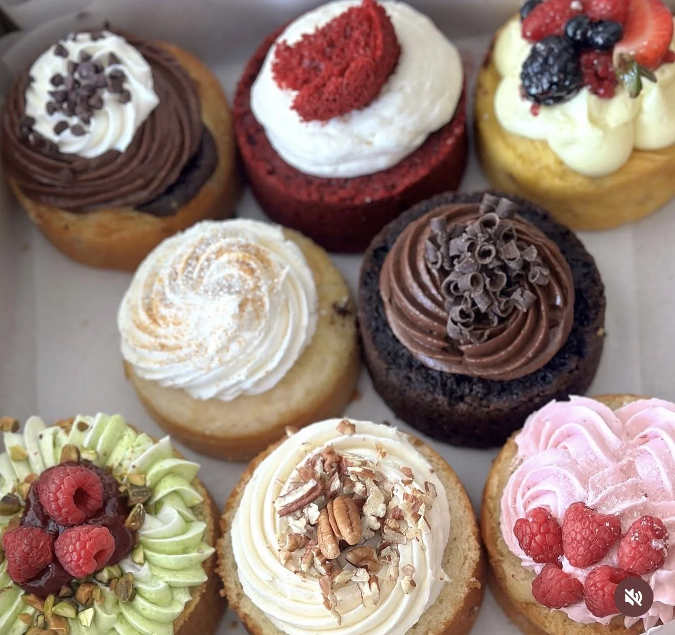 Assorted cupcakes decorated with frosting and fruits, including raspberries, blackberries, strawberries, and nuts.