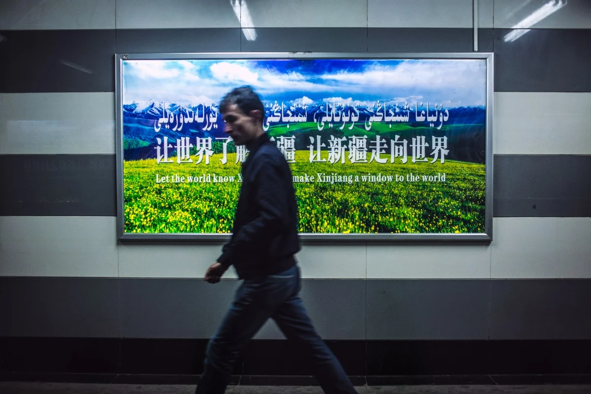 A Uyghur young man walks by a government sponsored sign promoting Xinjiang economic development.