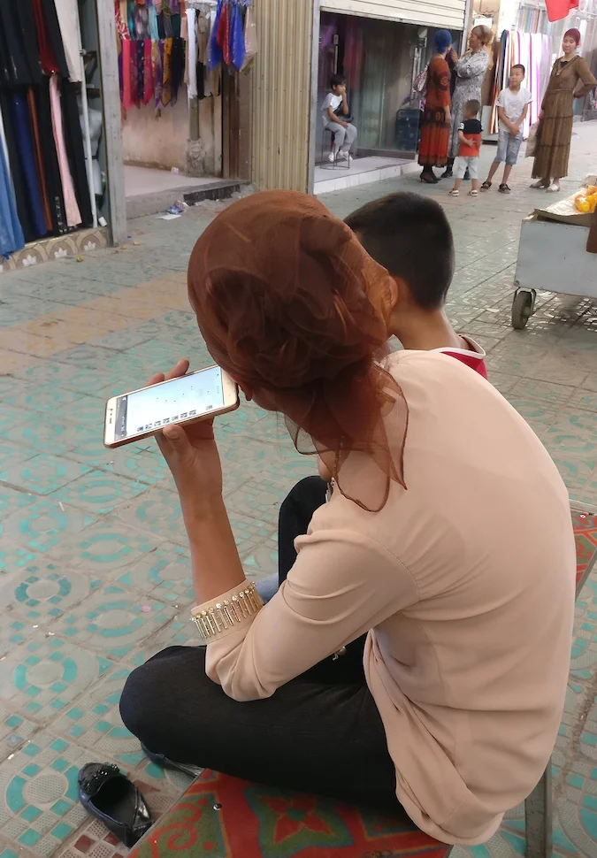 A woman who owns a woman's clothing shop in a rural bazaar sits listens to the messages of a WeChat group.