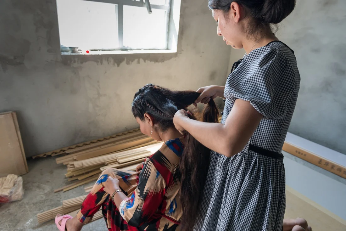 Gulnar begins to braid her friend’s hair to soothe her crying during a very quiet private conversation in an unfinished room of the family’s house.