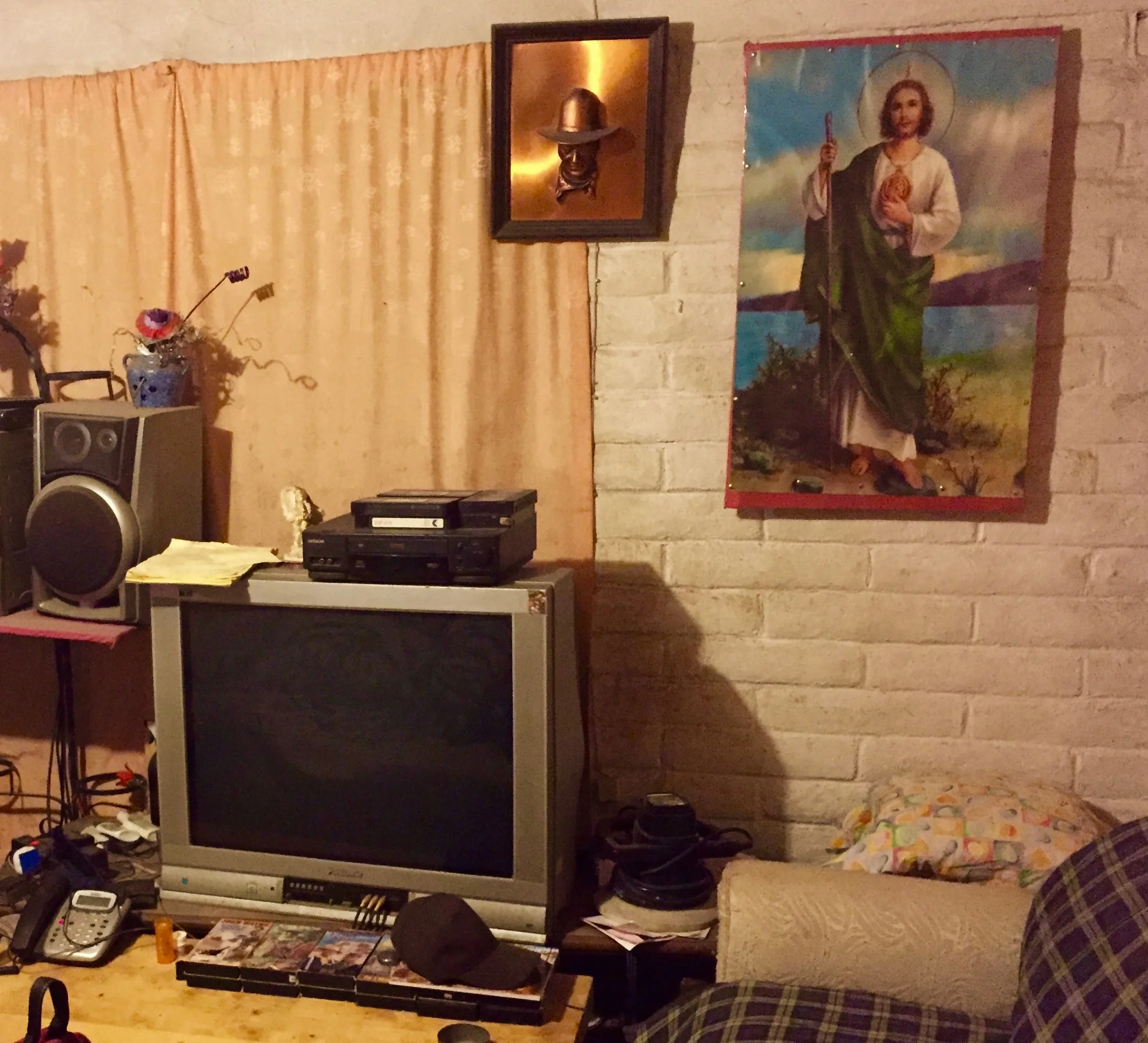Roy, deported after living in California for 47 years, has a copper engraving of American actor John Wayne on his living room wall in Nogales, Mexico. VHS copies of John Wayne films are stacked in front of his television. Photo credits: Tobin Hansen.