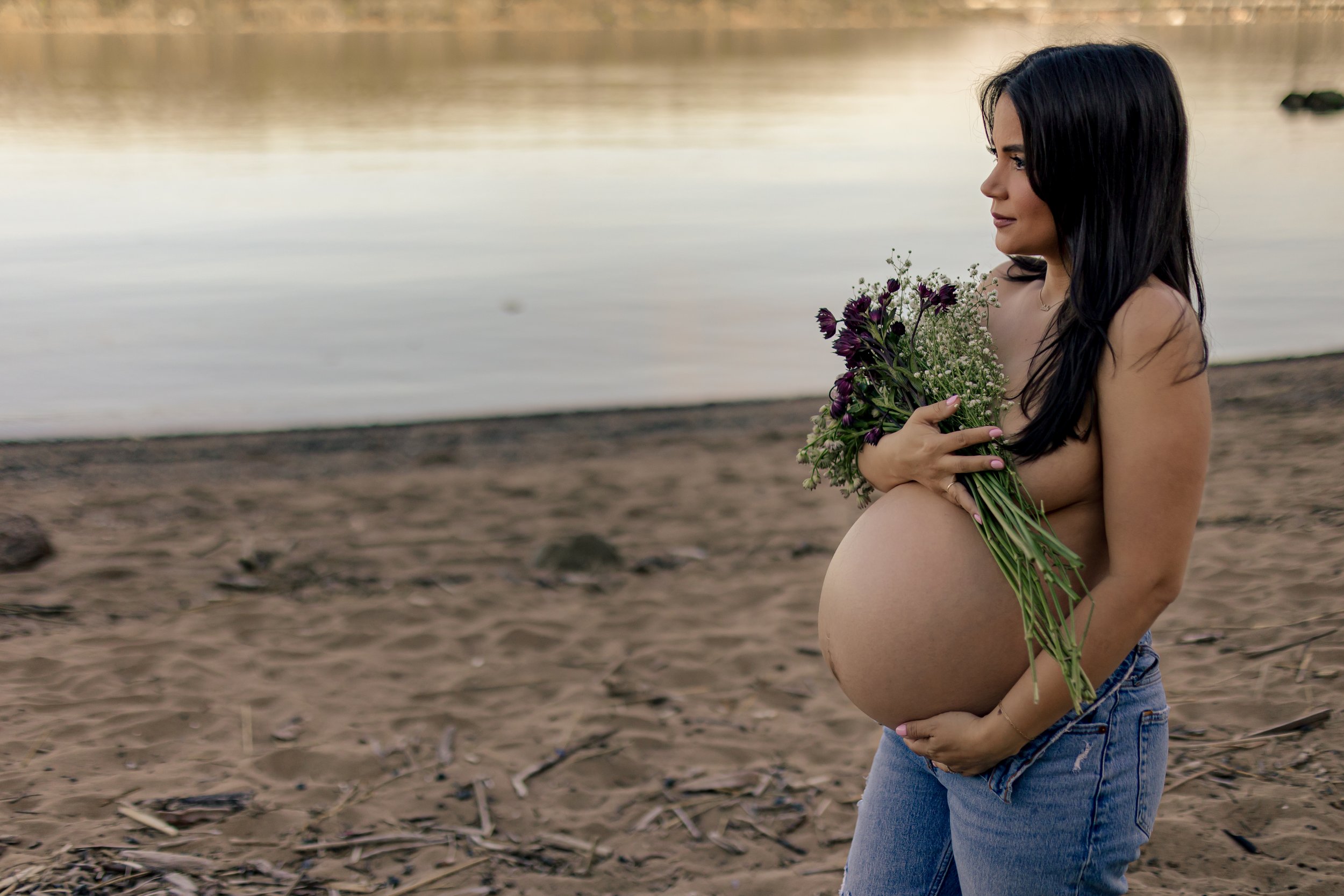 Pregnant woman holding flowers on a beach