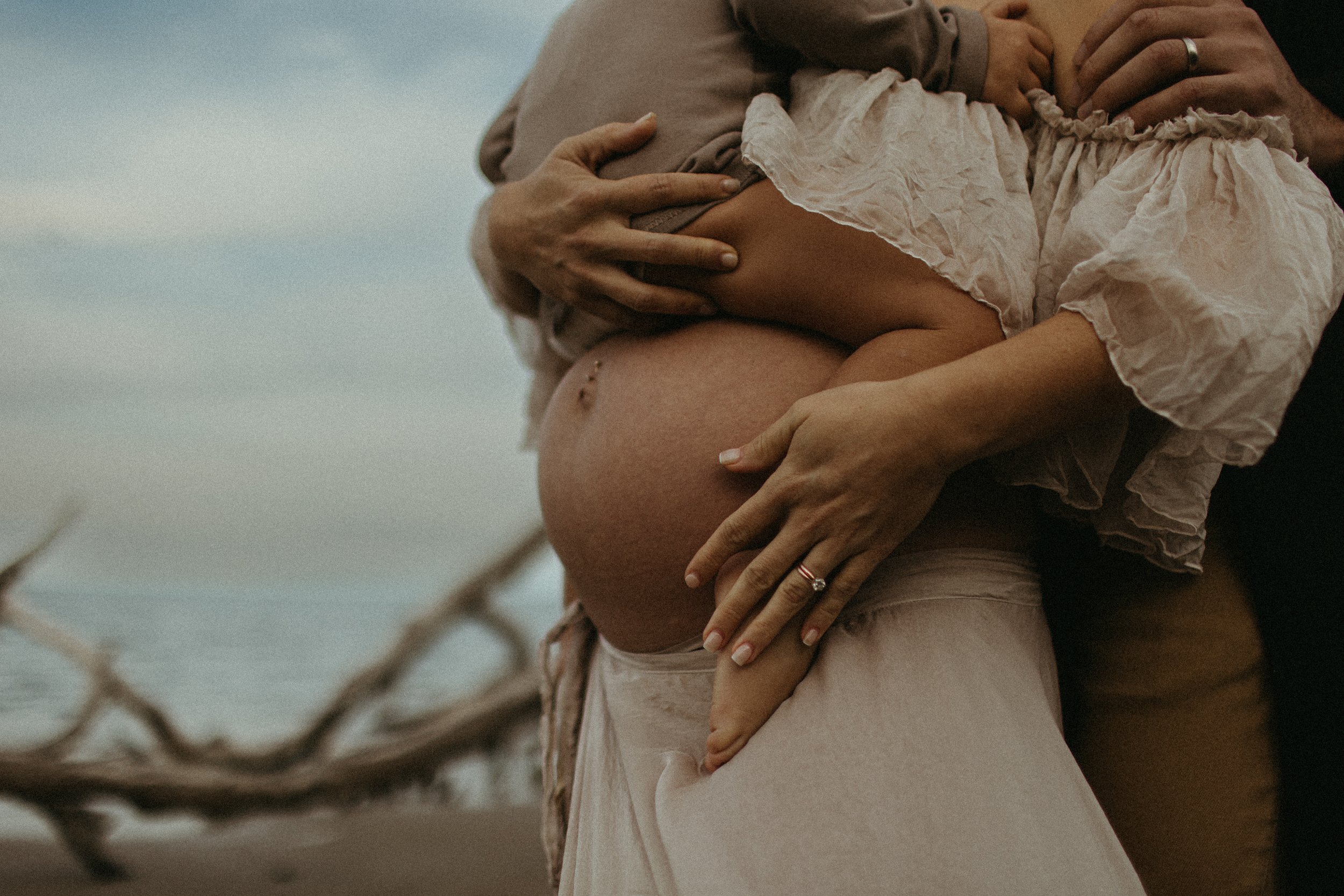 Pregnant woman on beach with family, close-up of belly and hands