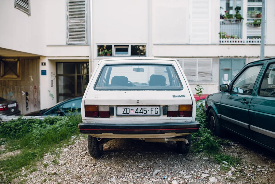 An old Yugoslav hatchback parked in front of one of the lackluster concrete apartment buildings in the city center.
