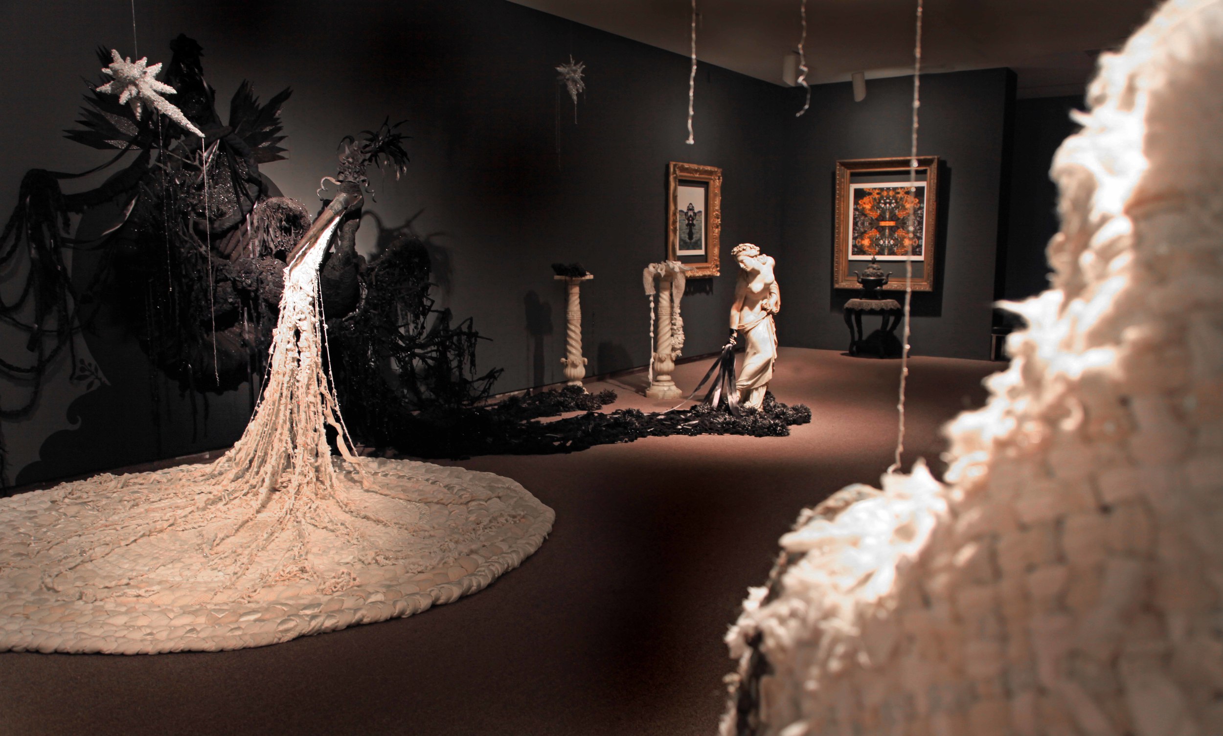 Then to the farthest realm in the galleries is the Celestial Realm , with charcoal walls and dramatic lighting on the glittering stars of the Seven Sisters from Dare alla Luce, reflected in another immense Eastlake-style mirror inlaid with mahogany and ebony. The center of this realm is filled with a massive intricate black Pelican Goddess enmeshed in 16 feet of black beaded crocheted tangles and paper chrysanthemums ,with yards of white beaded ‘milk’ flowing onto a 12 foot spiral referencing both an over-sized braided rag rug and a galaxy.