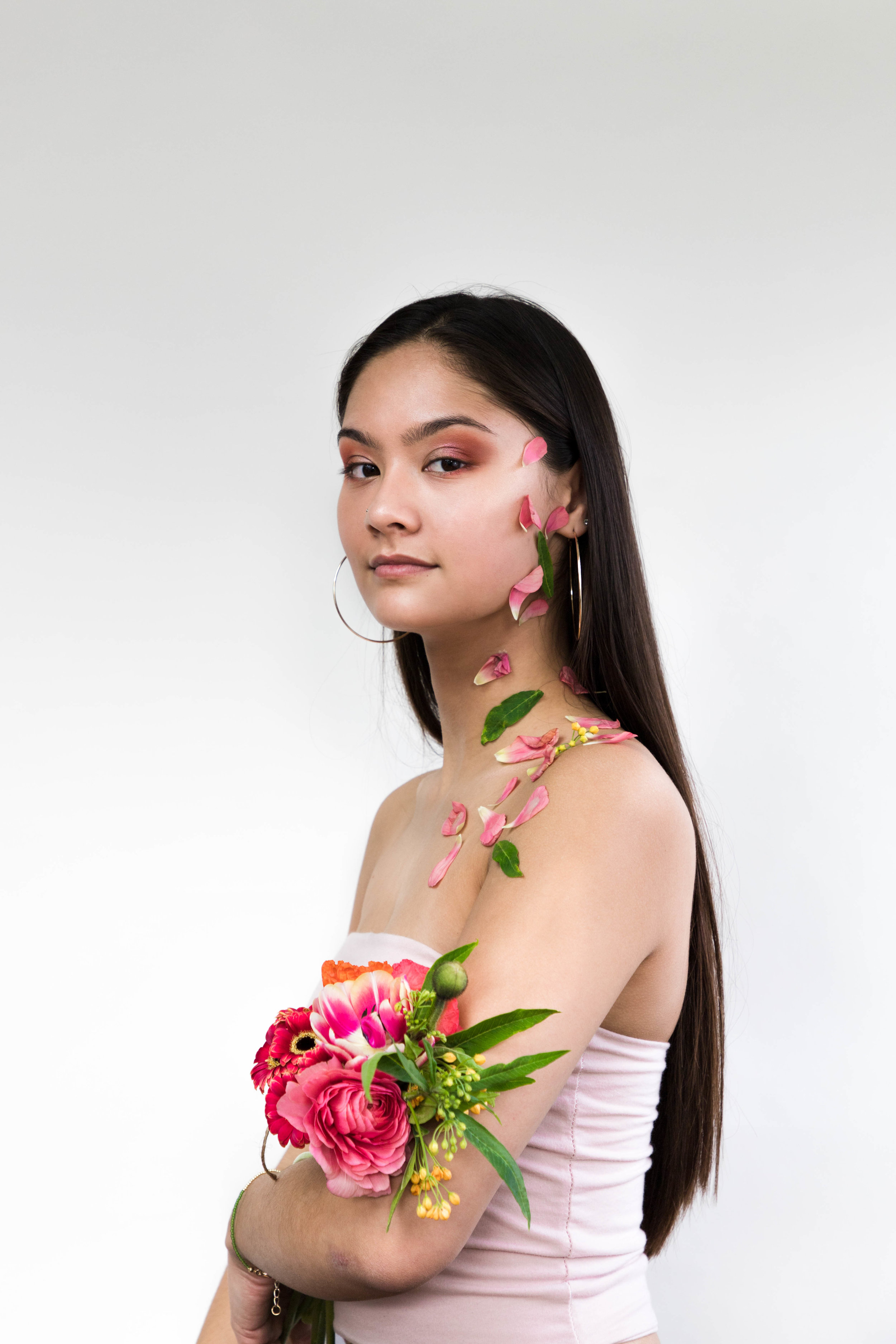  Woman against white background holding pink flowers with flower petals on her face 